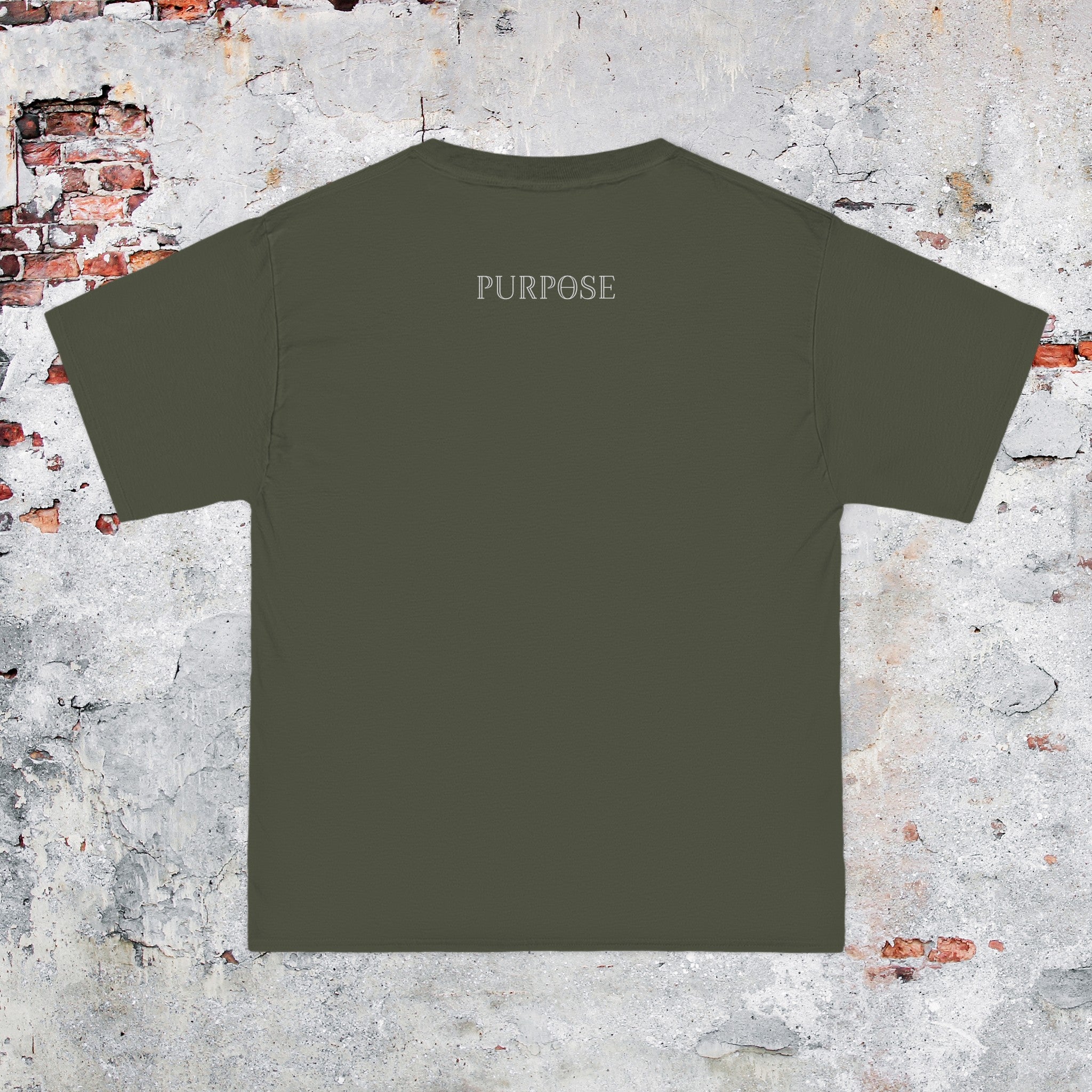 A roomy army green crewneck tee shirt displays the back of the garment as it lays against a painted brick-patterned wall. The Purpose worded logo is printed in white along the top center.