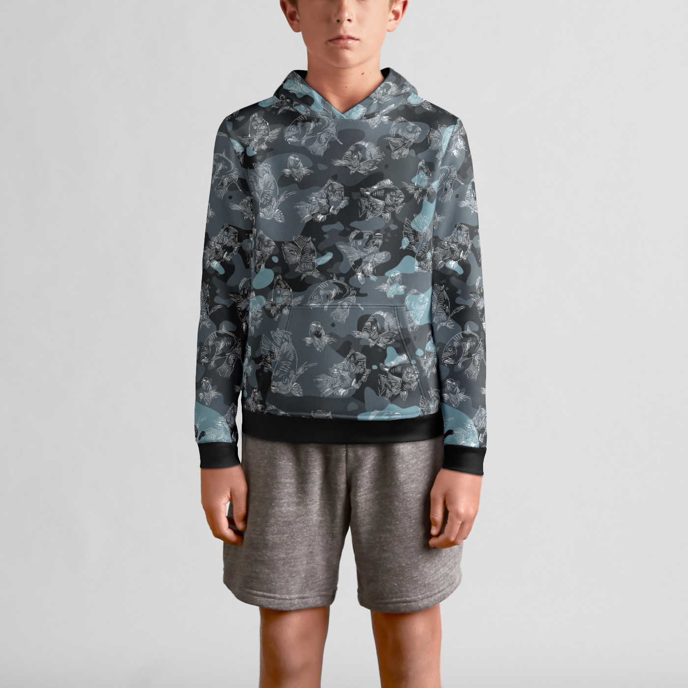 The front view of a male youth model in gray sweat shorts wearing a blue-camo hoodie with a white, all-over print line drawing of swimming carp. The hoodie has ribbed banding along the cuffs and bottom, and a kangaroo pocket in the front.