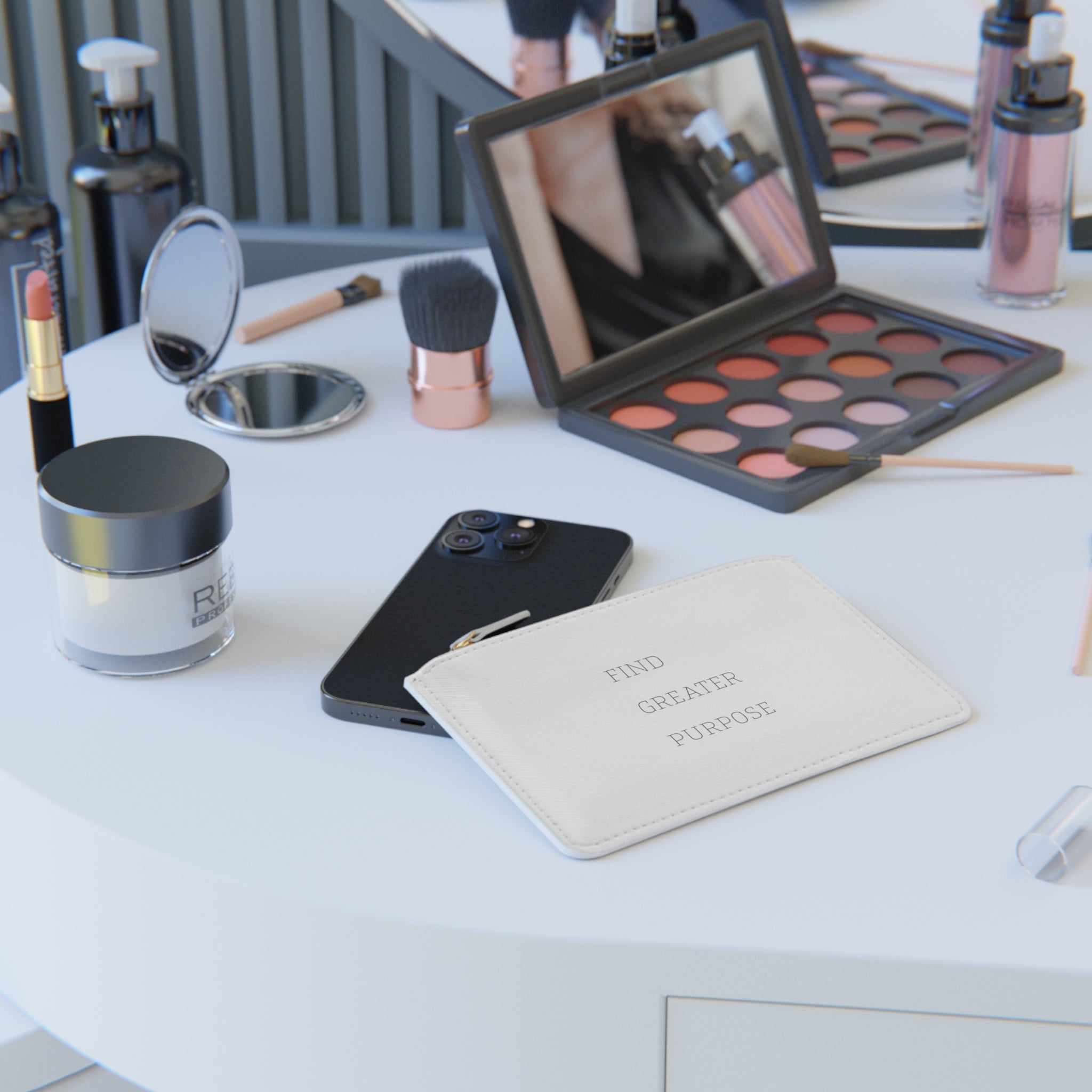 A table with an eyeshadow palette, makeup brushes, lipstick, hand mirror, various lotion bottles, and cell phone are displayed on a round table next to the white rectangular clutch with FIND GREATER PURPOSE in a simple serif font on the back.