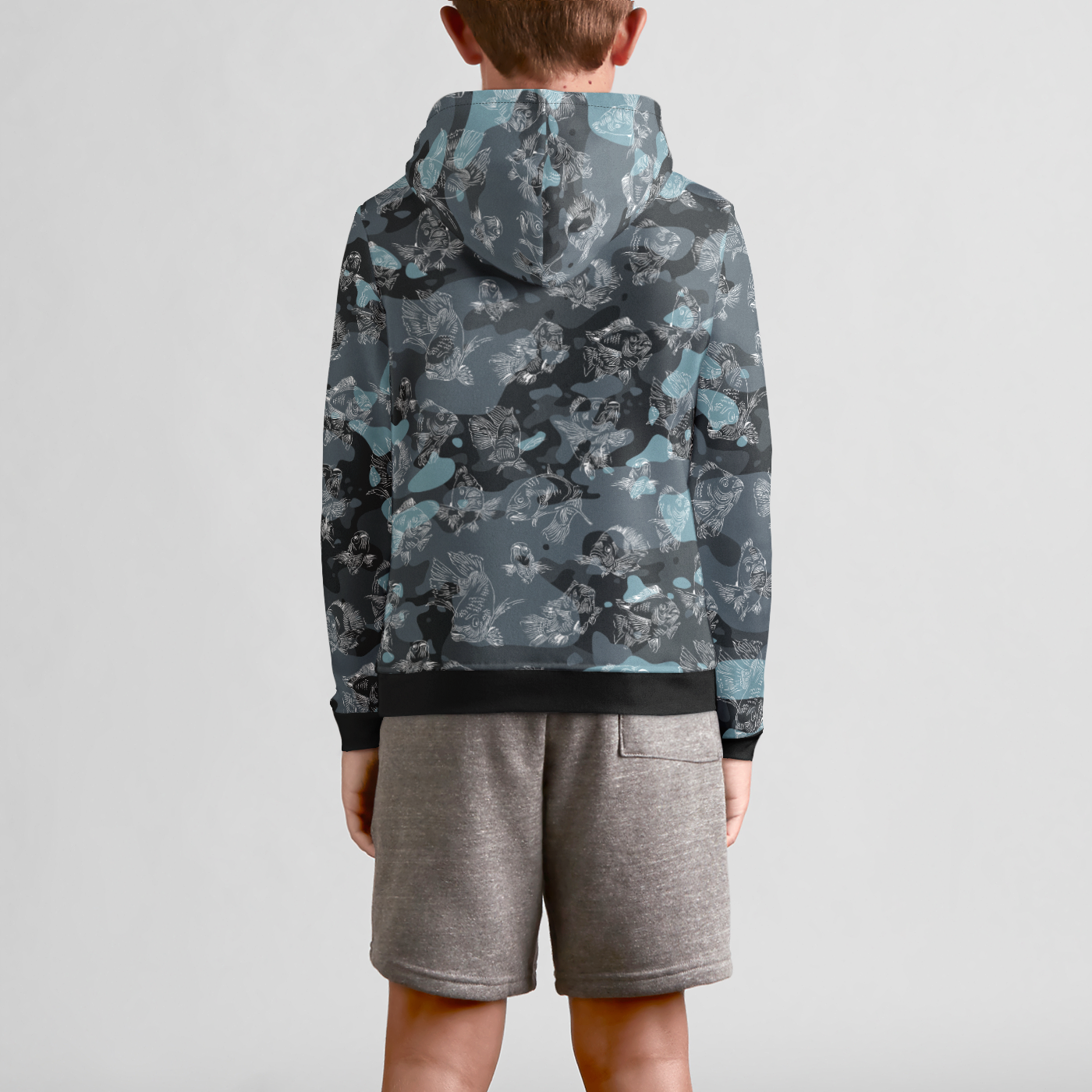 The back view of a male youth model in gray sweat shorts wearing a blue-camo hoodie with a white, all-over print line drawing of swimming carp. The hoodie has ribbed banding along the cuffs and bottom, with the pattern repeated on the hood.