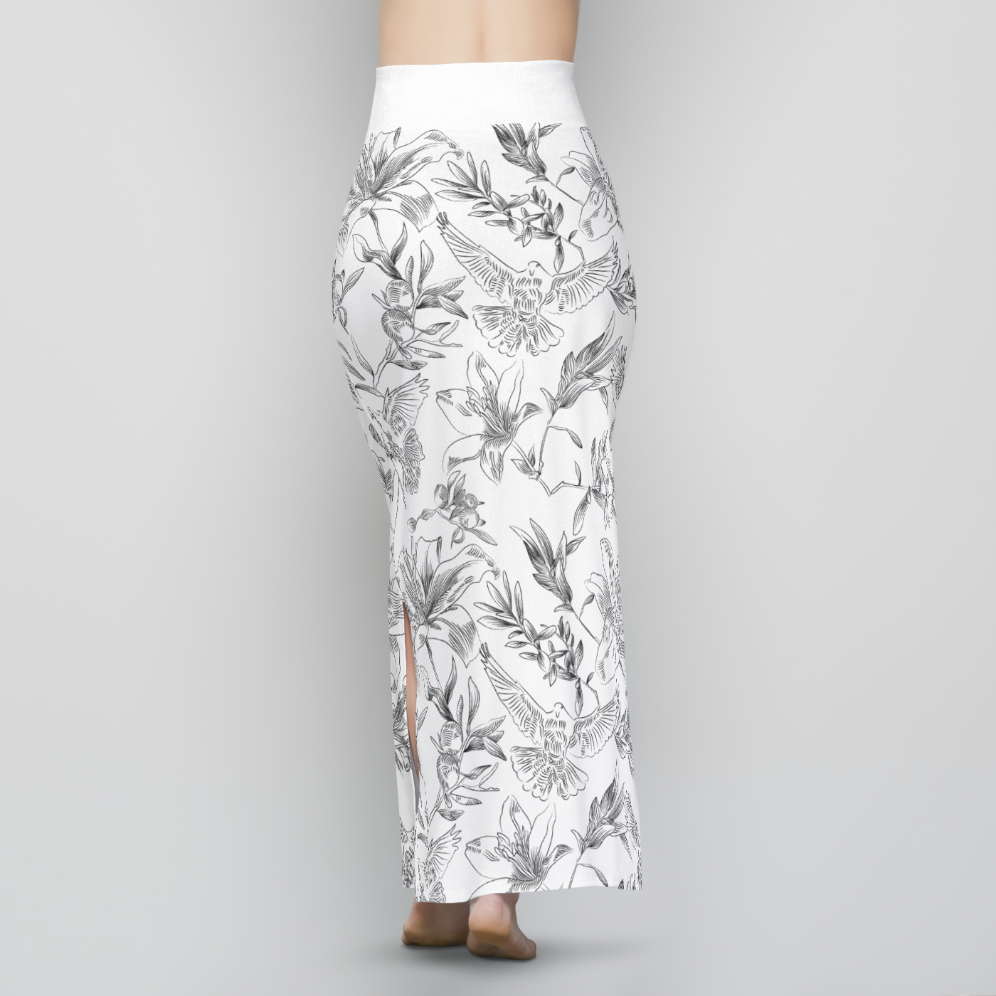 The back, lower half of a female model wearing a long, white, sheath-style, maxi skirt with a black line-drawing pattern of doves, flowers, and olive branches. The skirt is high-waisted with a wide, white band of fabric at the waist.