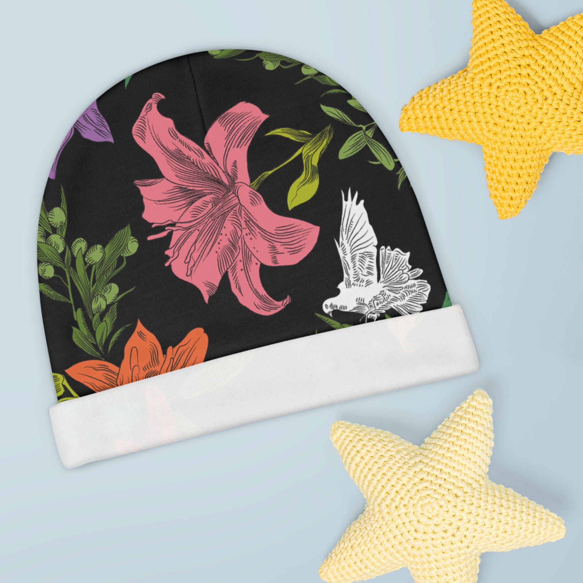 A black, knit, baby beanie with multi-colored, all-over print of doves, flowers, and olive branches, displaying a white folded brim.