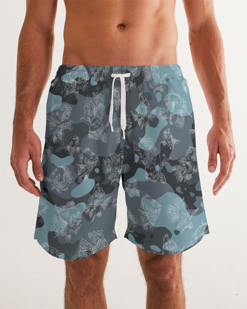 A close-up of a male model wearing a pair of blue camo board shorts with an all-over swimming carp print in a white pattern, with a white exterior drawstring loosely knotted. 