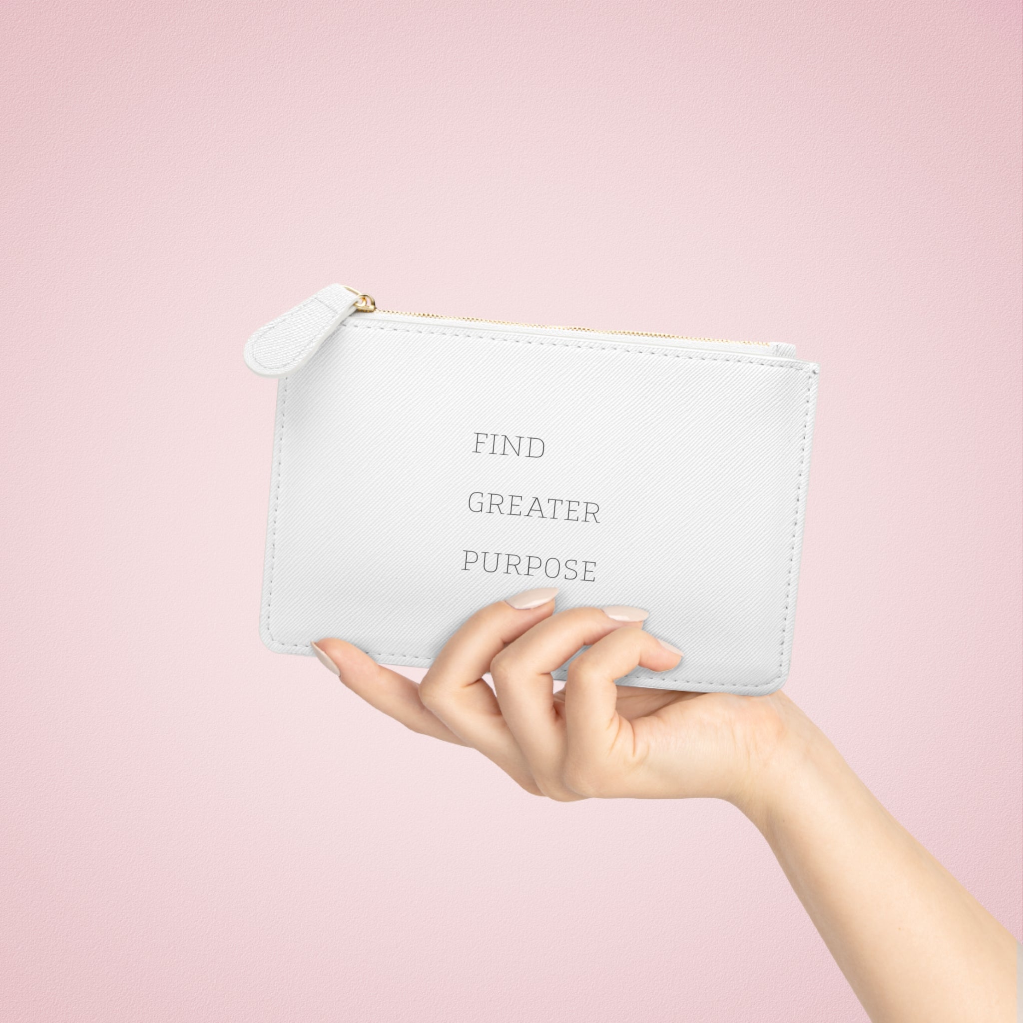 A nicely manicured female hand is displaying the back of a 6.3 inch by 4 inch white clutch. The words on the back read FIND GREATER PURPOSE in a clean and simple serif font.