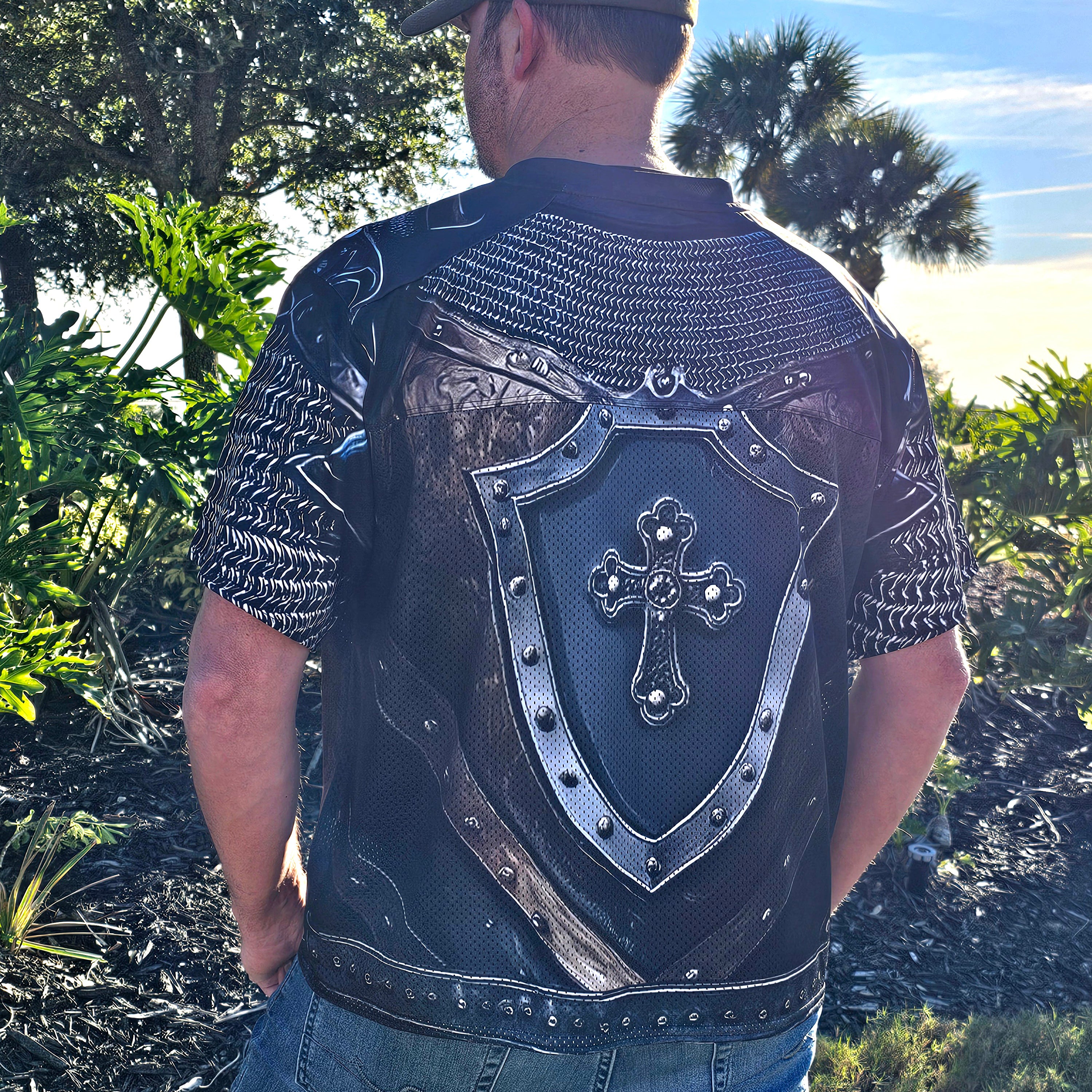 Person wearing a decorative black shirt with armor-like design and cross emblem outdoors.