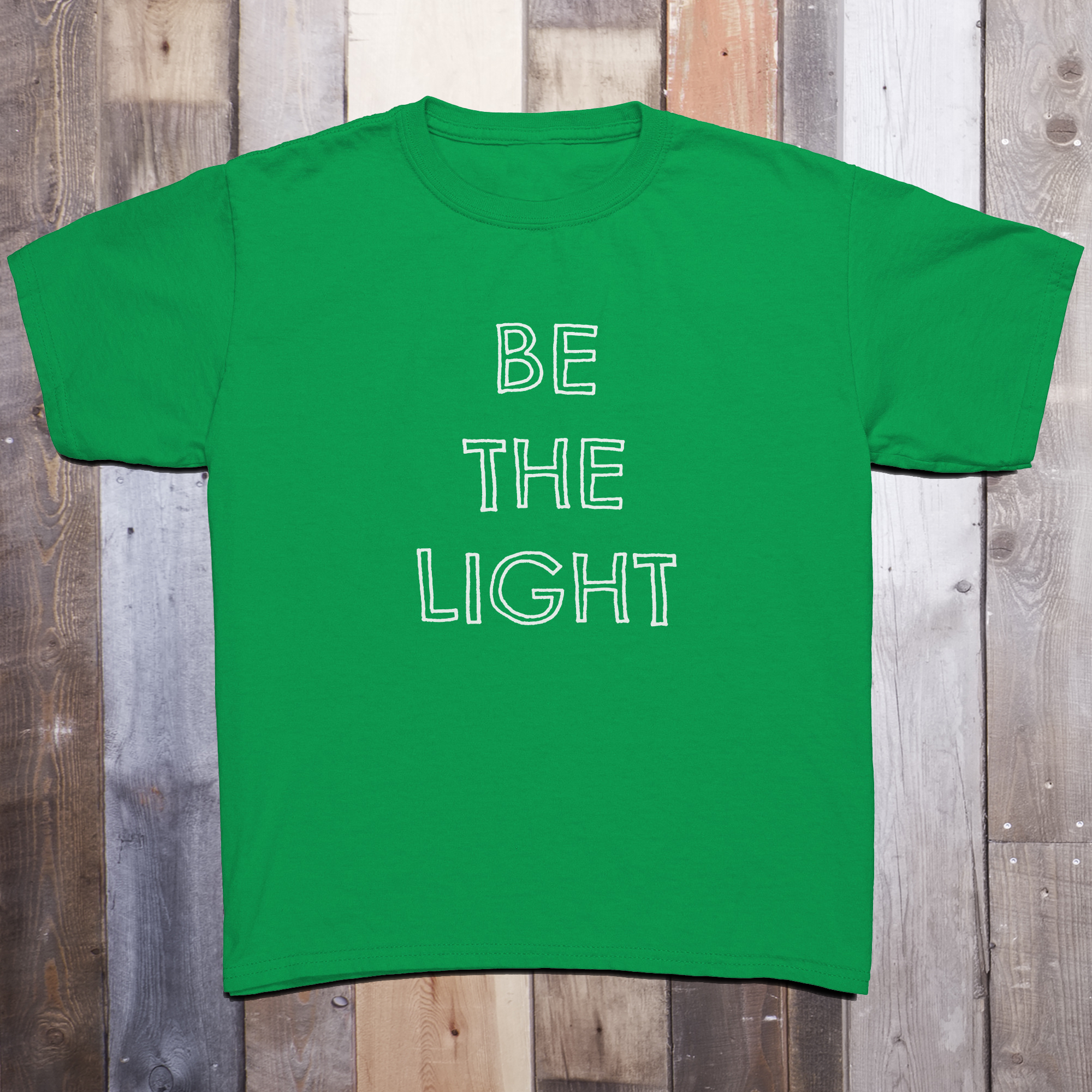 Green t-shirt with the phrase BE THE LIGHT written in white on the front center of the garment, with each word stacked above the other.