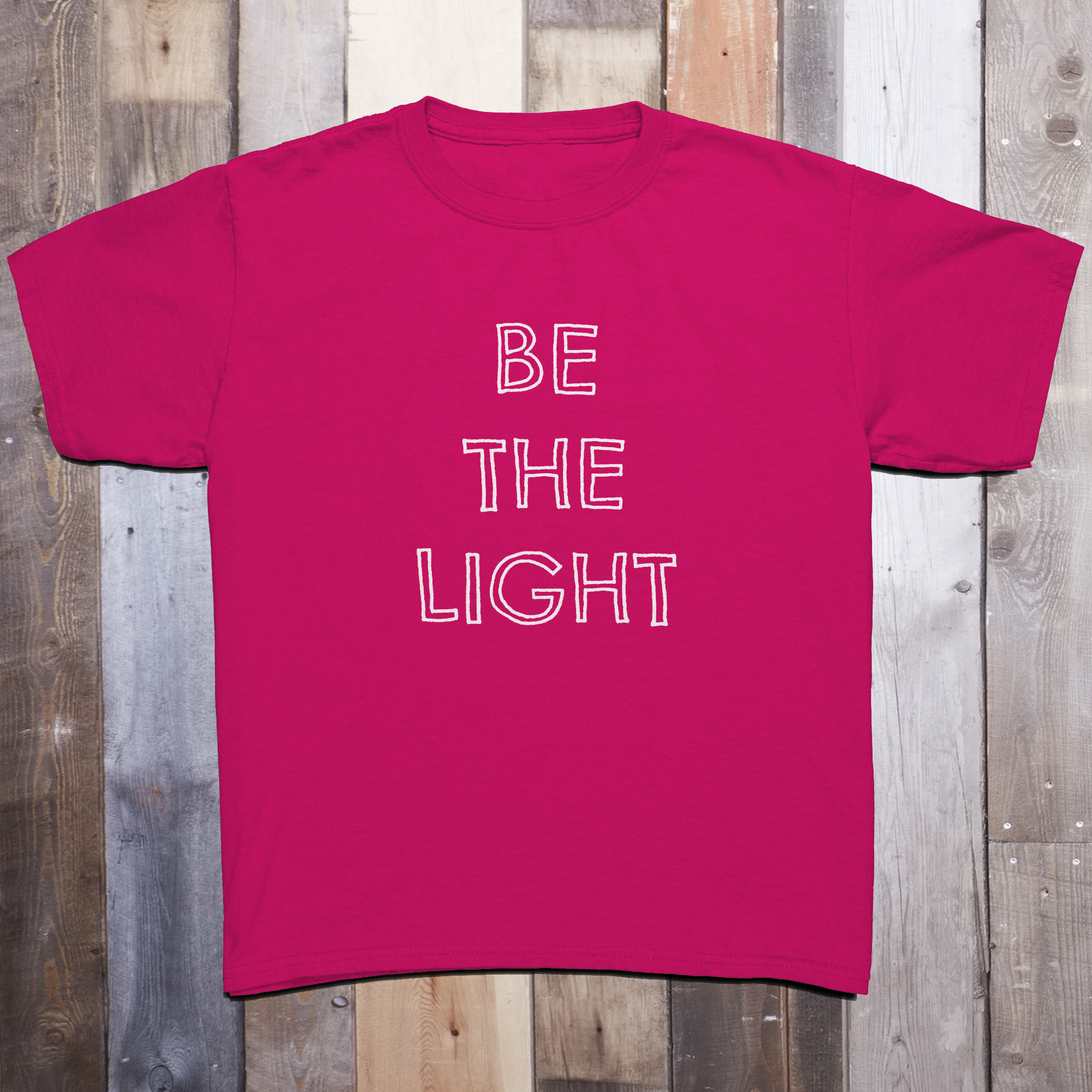 Bright pink t-shirt with the phrase BE THE LIGHT written in white on the front center of the garment, with each word stacked above the other.