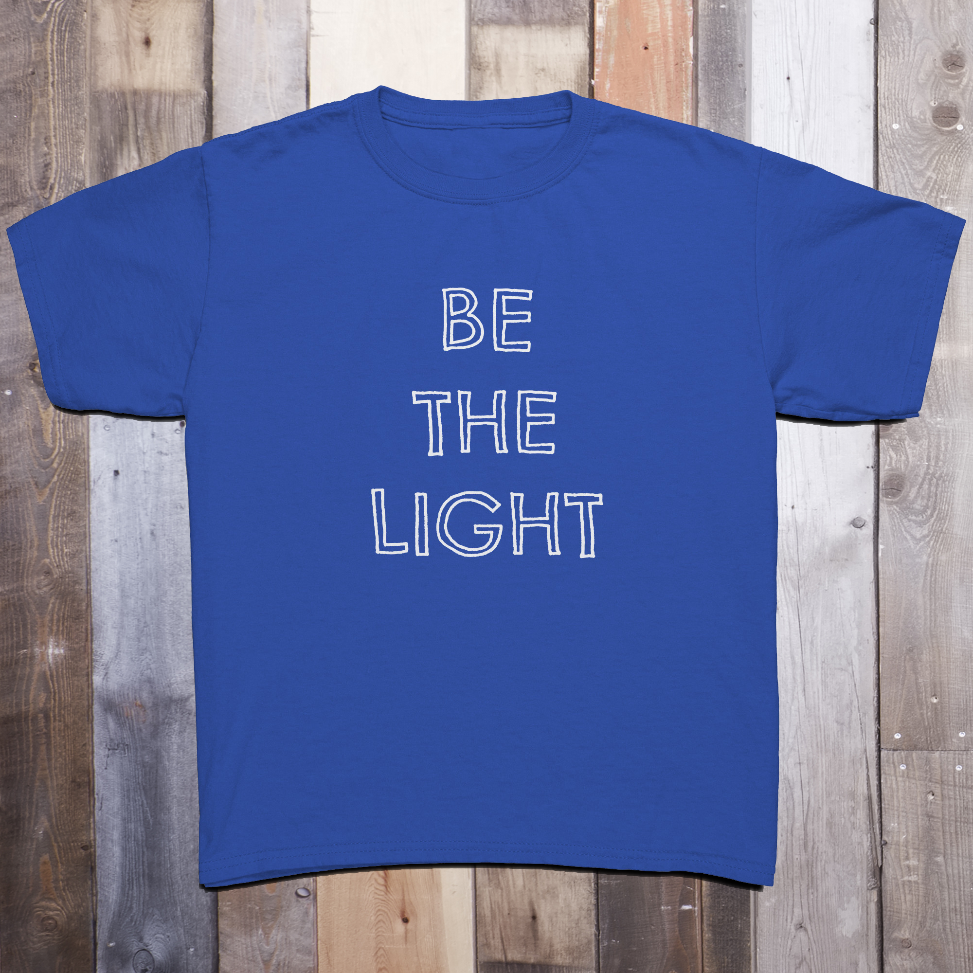 Blue t-shirt with the phrase BE THE LIGHT written in white on the front center of the garment, with each word stacked above the other.