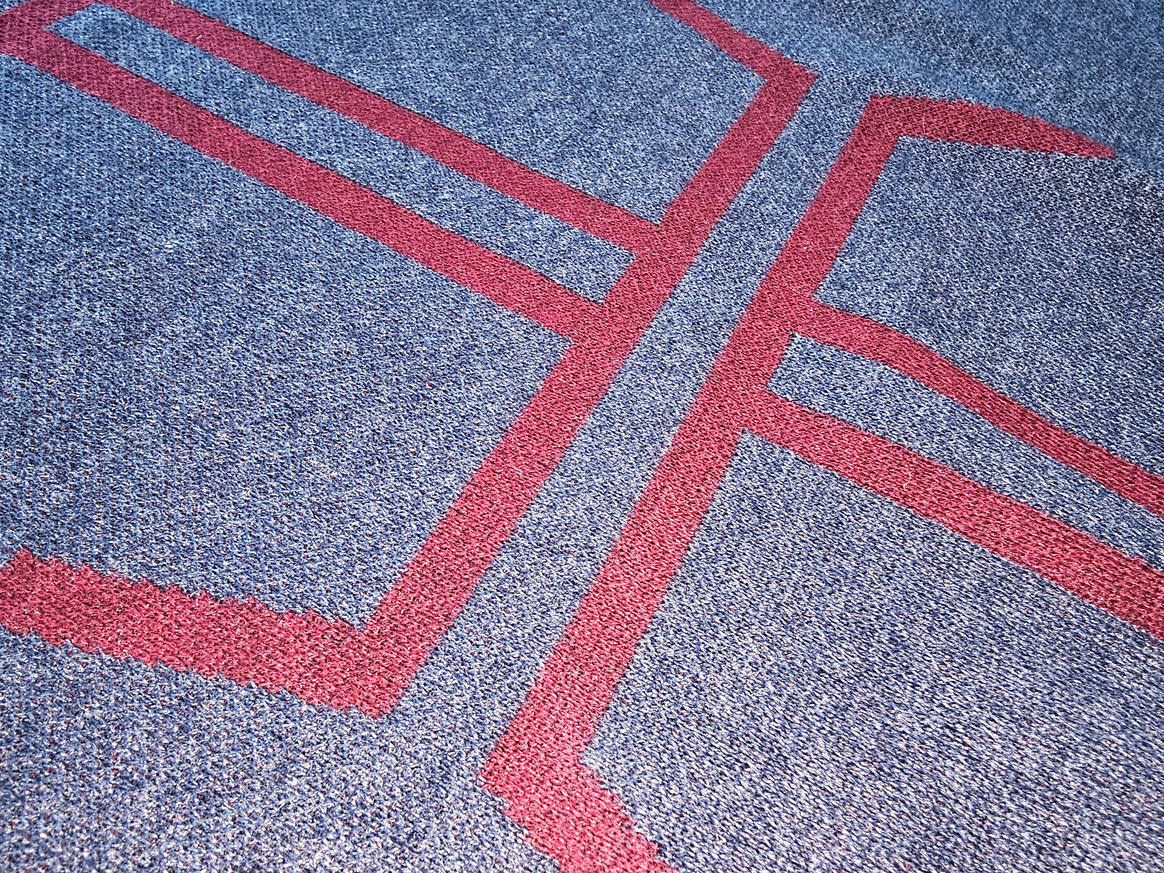 An angled close-up of the burgundy knitted cross graphic on the sweater chest.