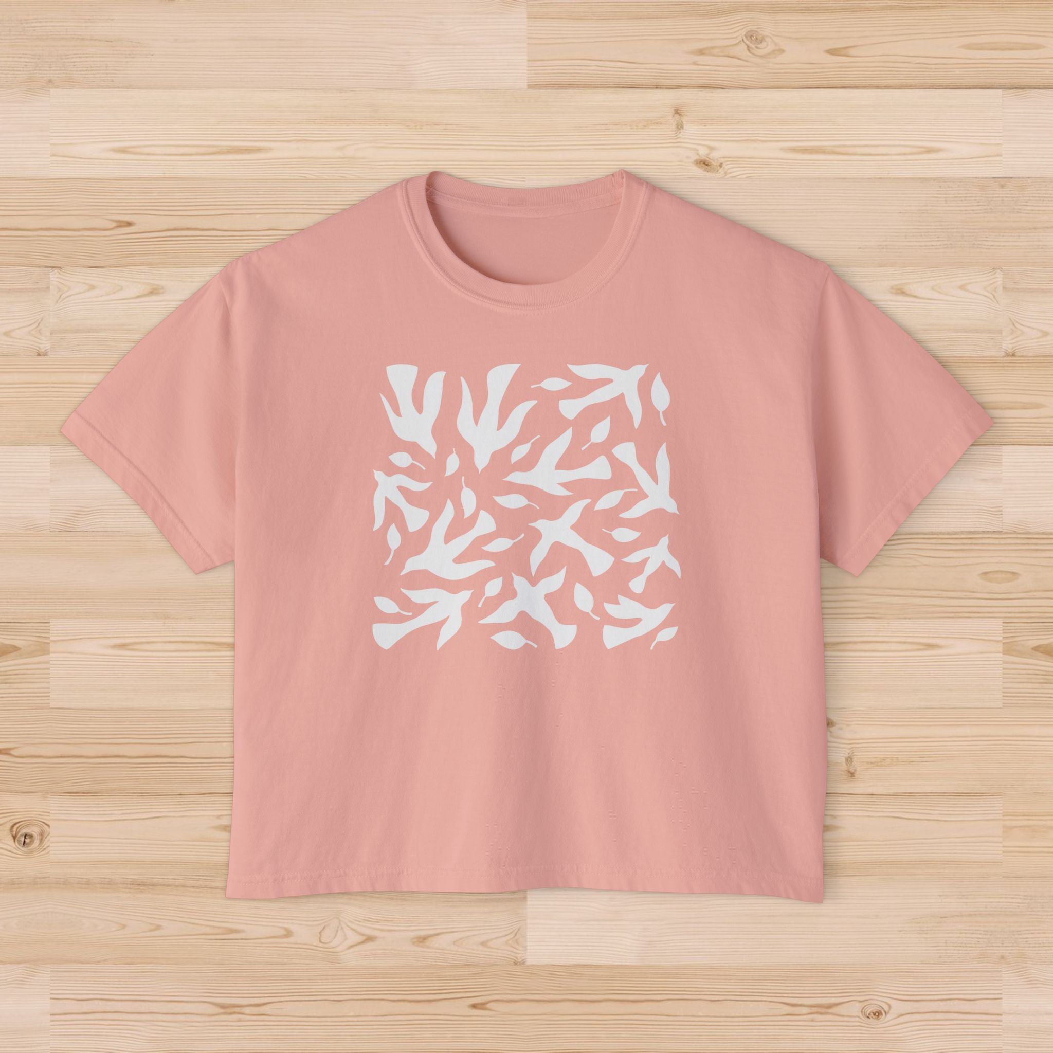 Peach-colored t-shirt with white abstract dove pattern on a wooden surface