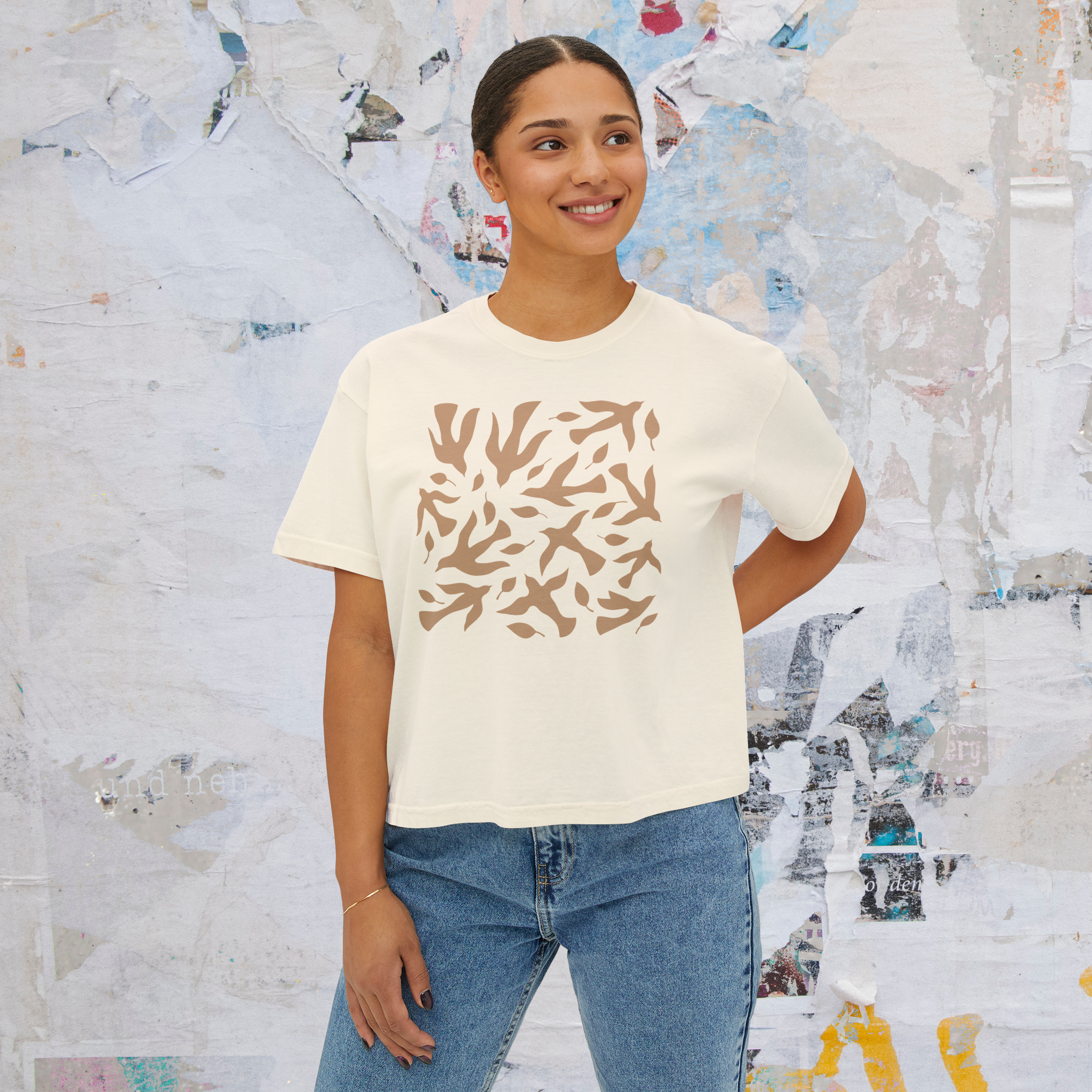 Woman wearing a cream t-shirt with a brown abstract pattern and blue jeans on a white background. Christian T-shirt.