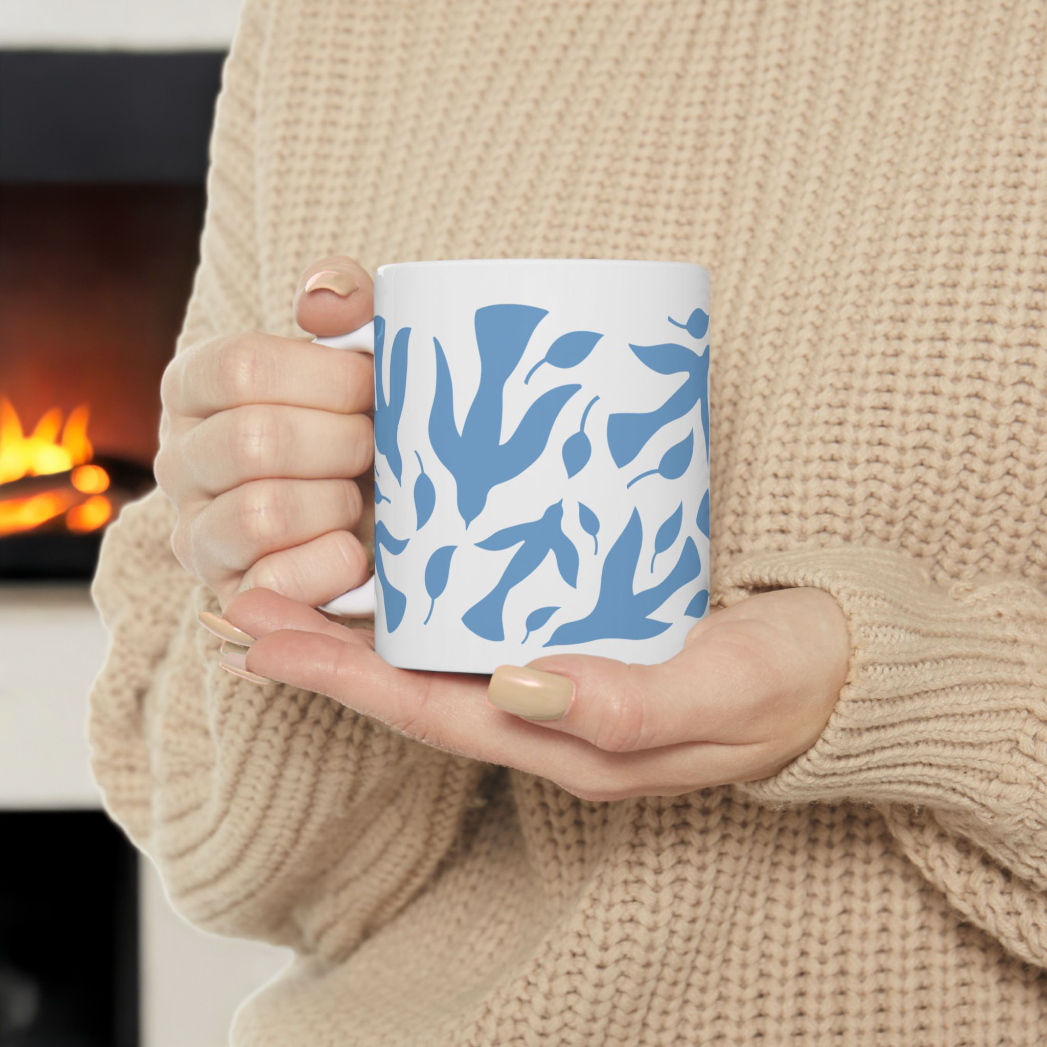 Woman holding a white mug with blue dove and leaf pattern in front of a fireplace