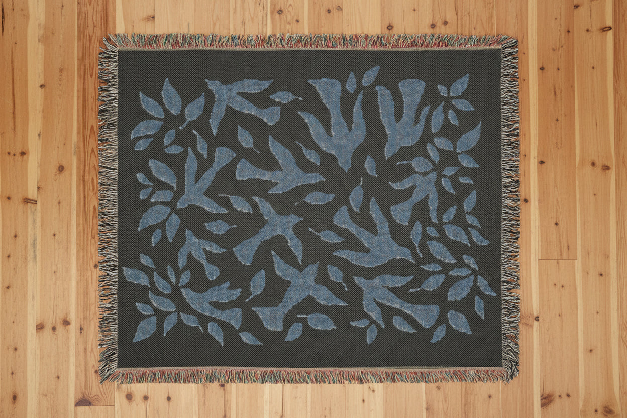 Black blanket with blue leaf and dove pattern against a dark background on a wood floor