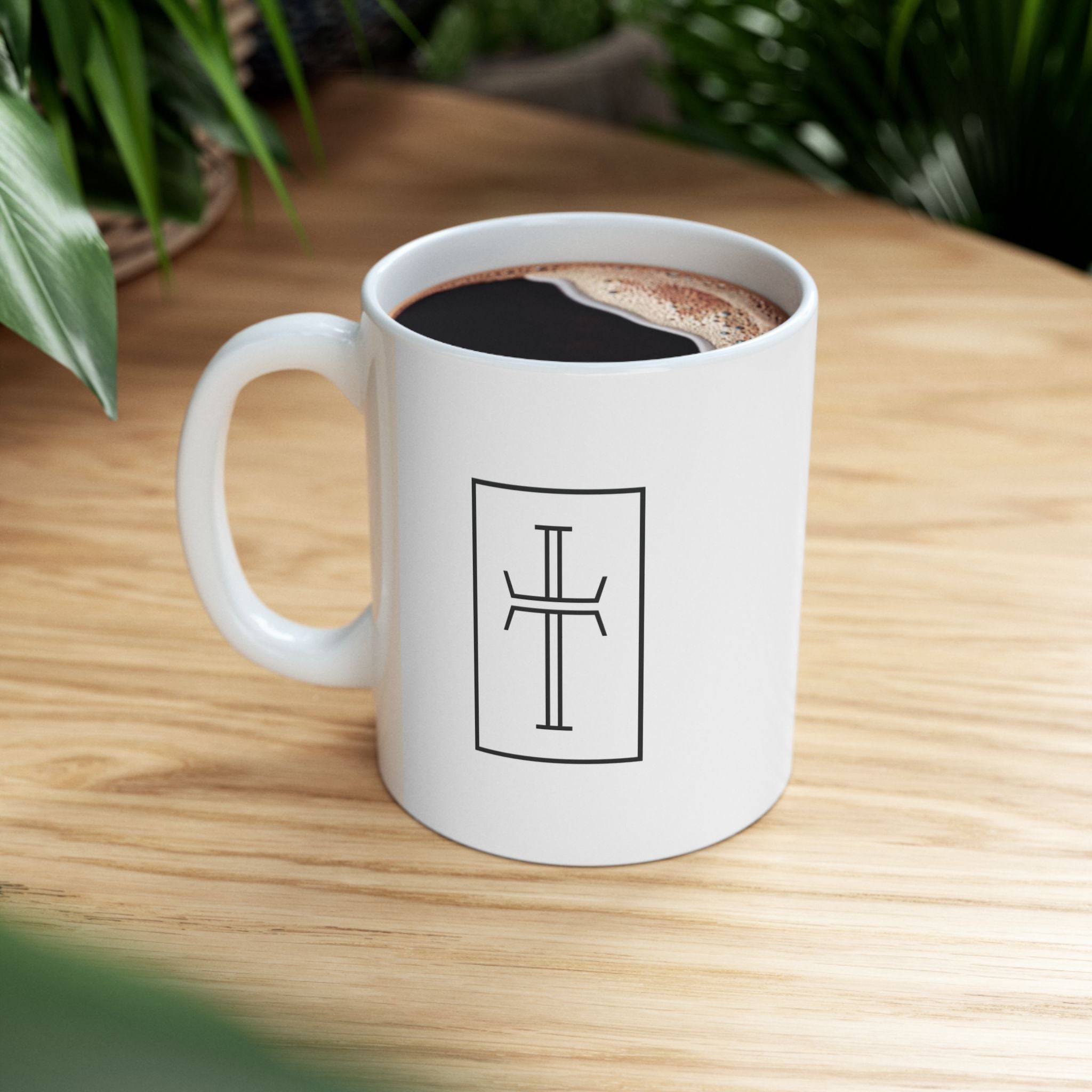 White mug with a black cross on a wooden table.