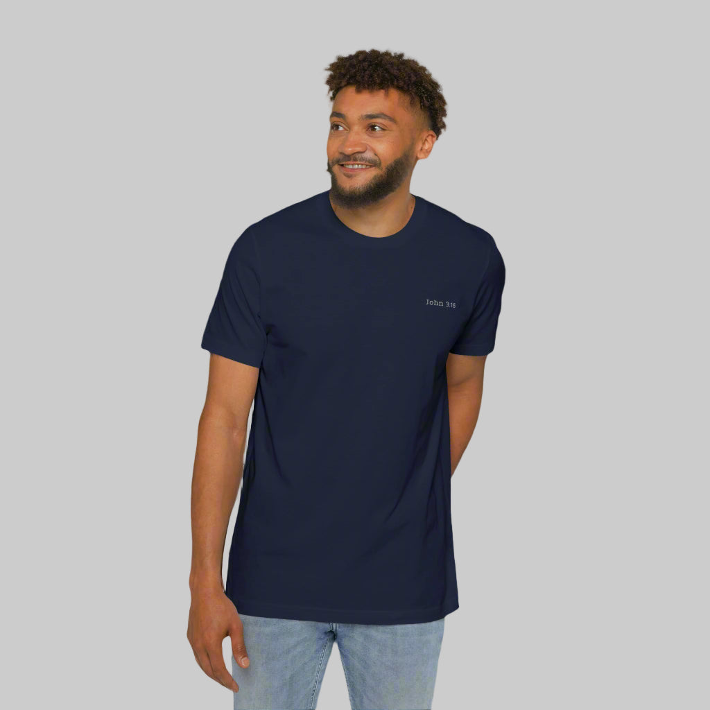 The front side of a male model wearing blue jeans and a navy tee shirt with the bible verse John 3:16 written in white on the left chest.
