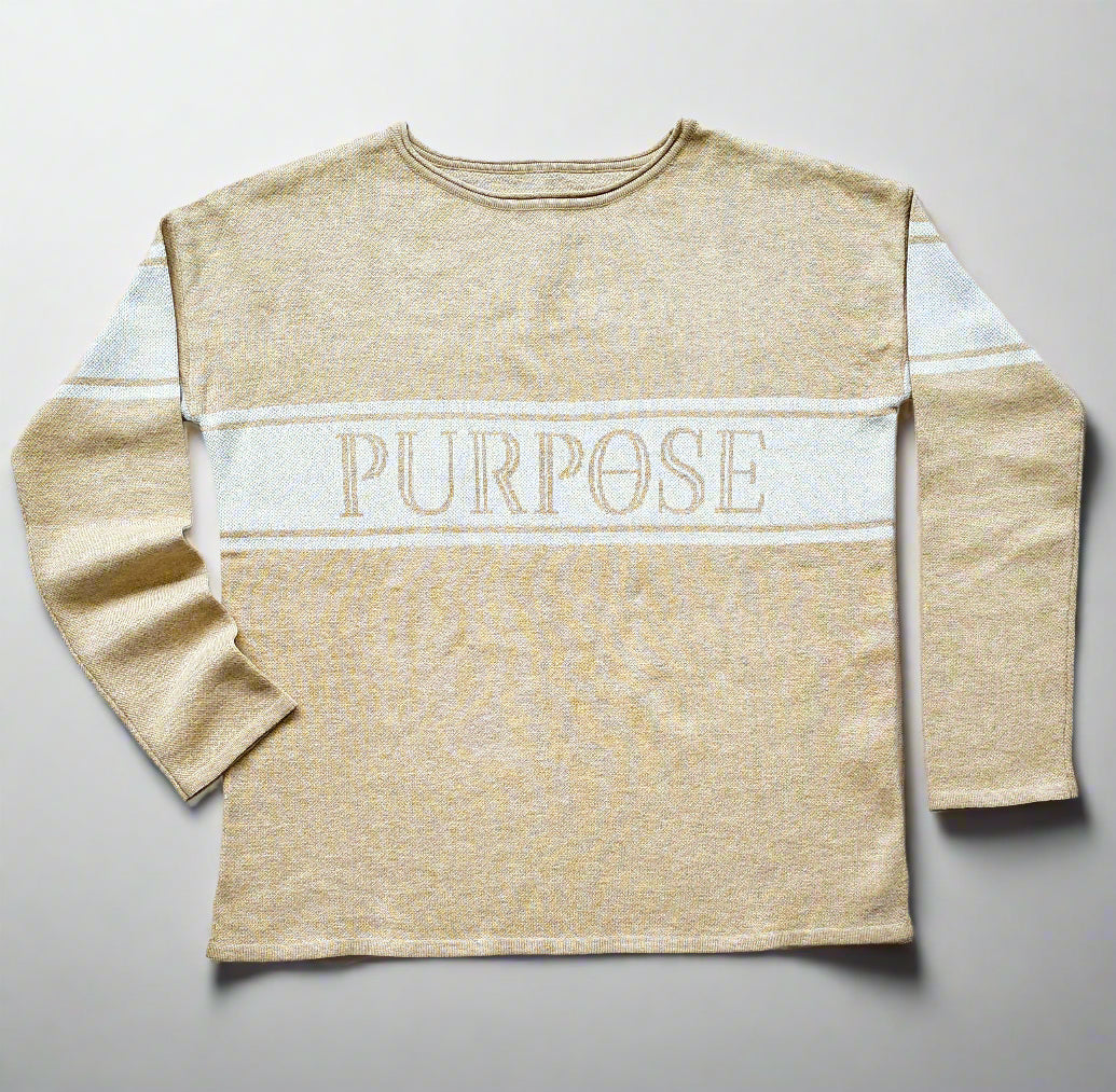 The beige sweater with two narrow white stripes and wide center stripe along the chest and upper arms, is displayed against a white background. The word "Purpose" is written in large, beige, capital letters on the center chest stripe.