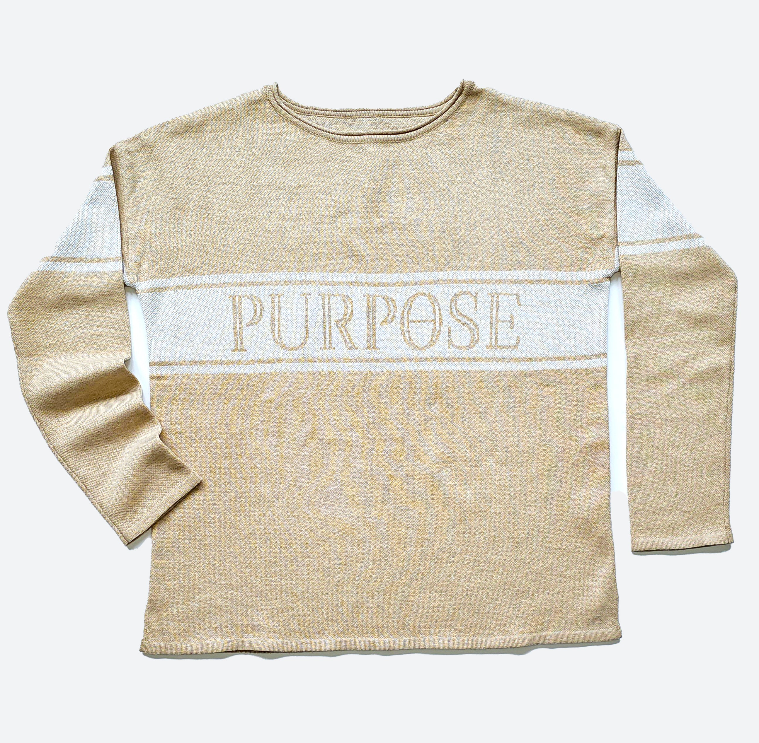 The beige sweater with two narrow white stripes and wide center stripe along the chest and upper arms, is displayed against a white background. The word "Purpose" is written in large, beige, capital letters on the center chest stripe.