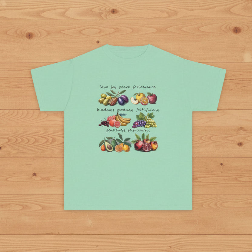 Light green t-shirt with fruit illustrations and Biblical fruit of the spirit text on a wood floor background