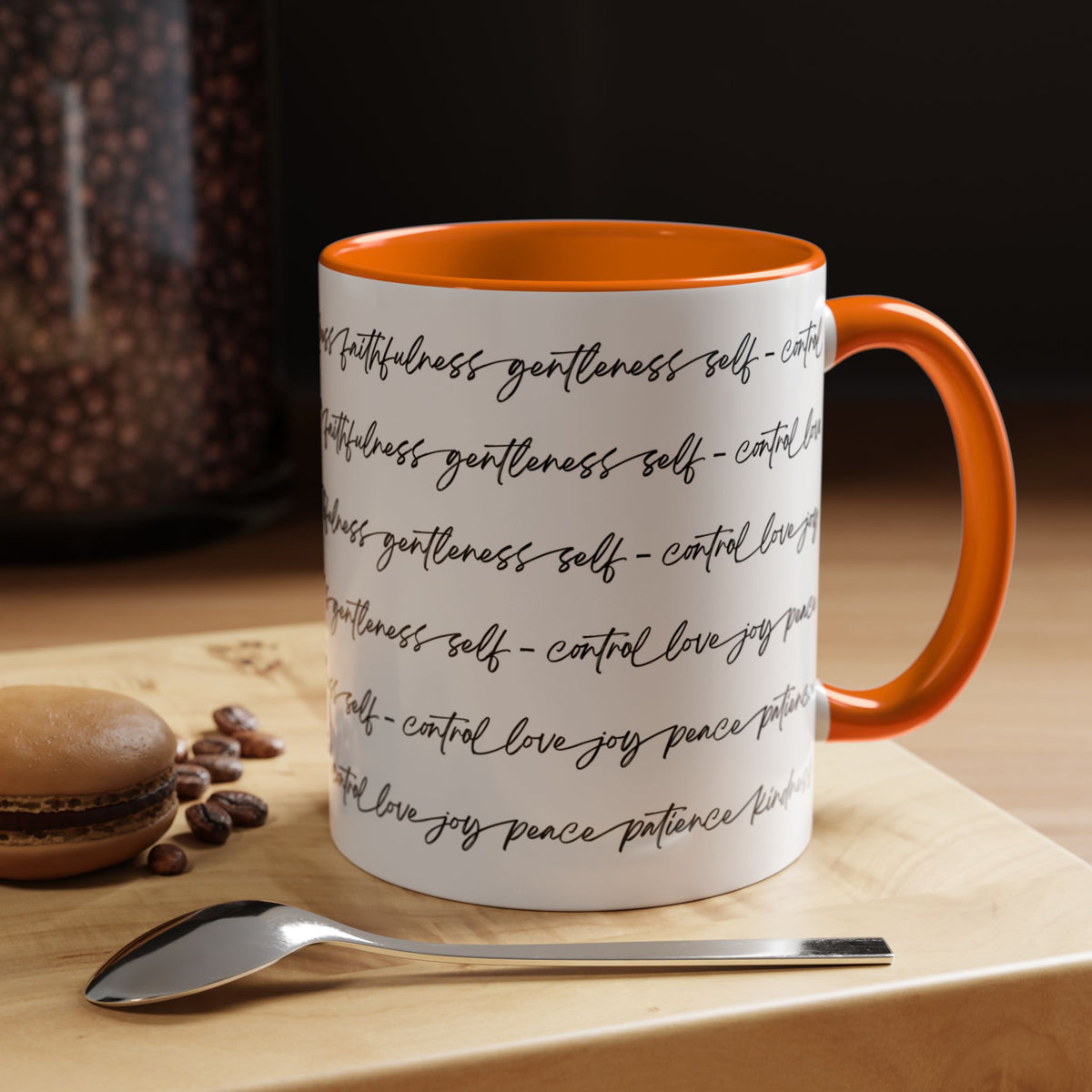 Right side of 11oz mug with orange interior and handle with black scripted text written on a white background sitting on a wooden surface with coffee beans and a spoon.
