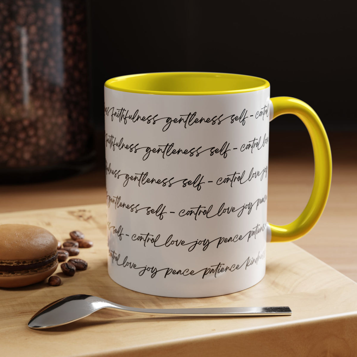 Right side of 11oz mug with yellow interior and handle with black scripted text written on a white background sitting on a wooden surface with coffee beans and a spoon.