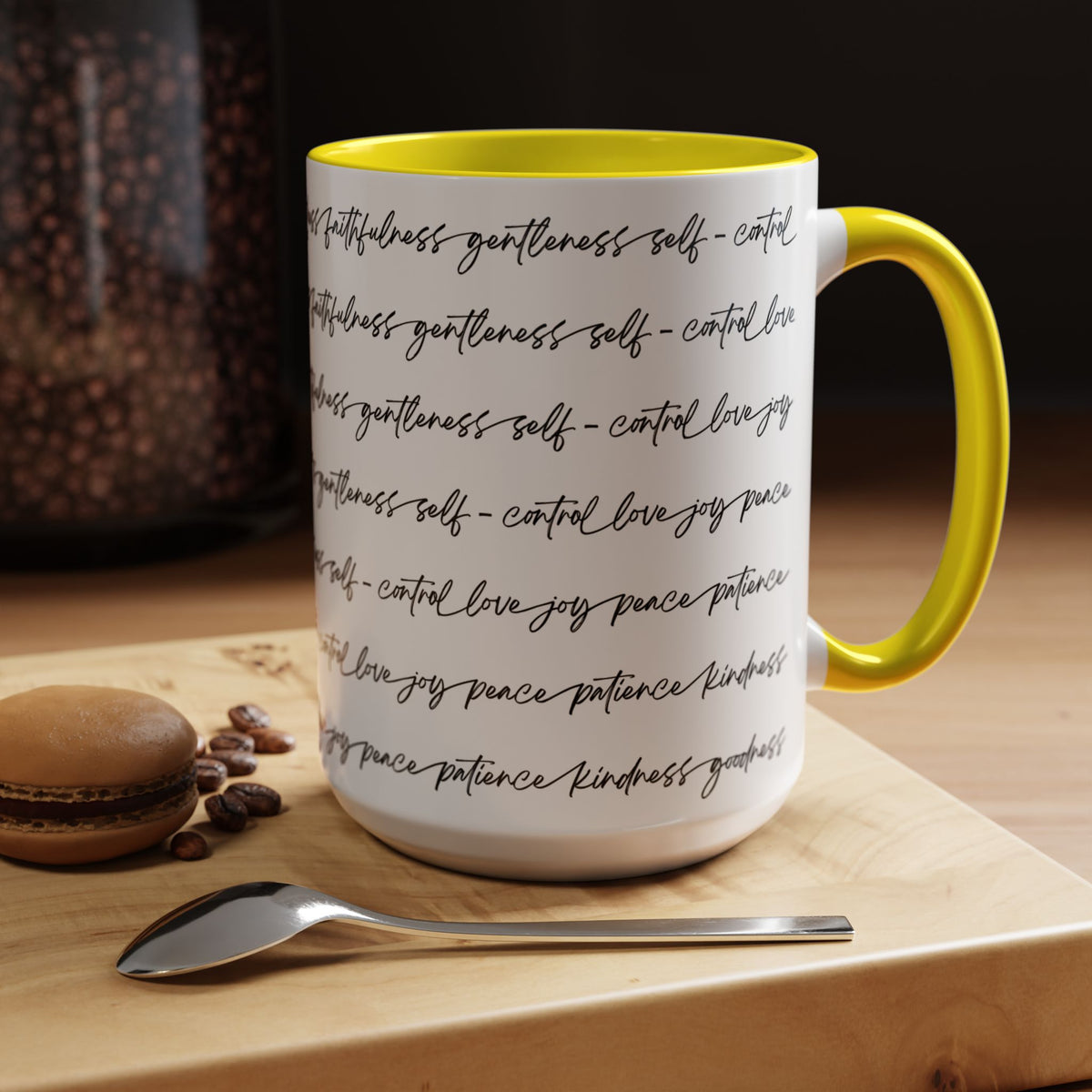 Right side of 15oz mug with yellow interior and handle with black scripted text written on a white background sitting on a wooden surface with coffee beans and a spoon.
