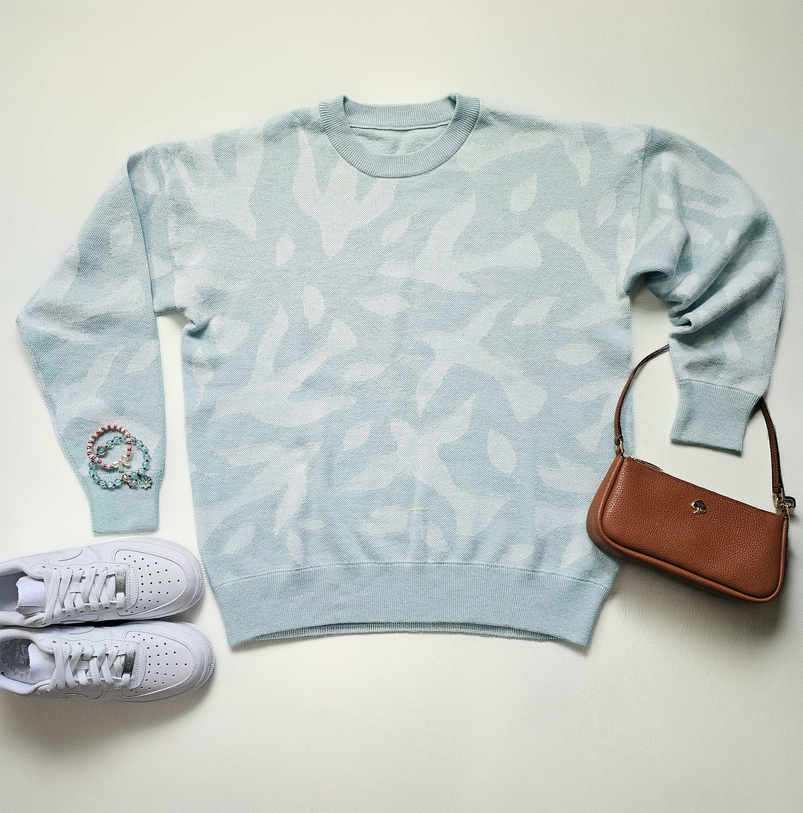 Light blue sweater with white dove and leaf pattern paired with white sneakers and a brown handbag on a light background.
