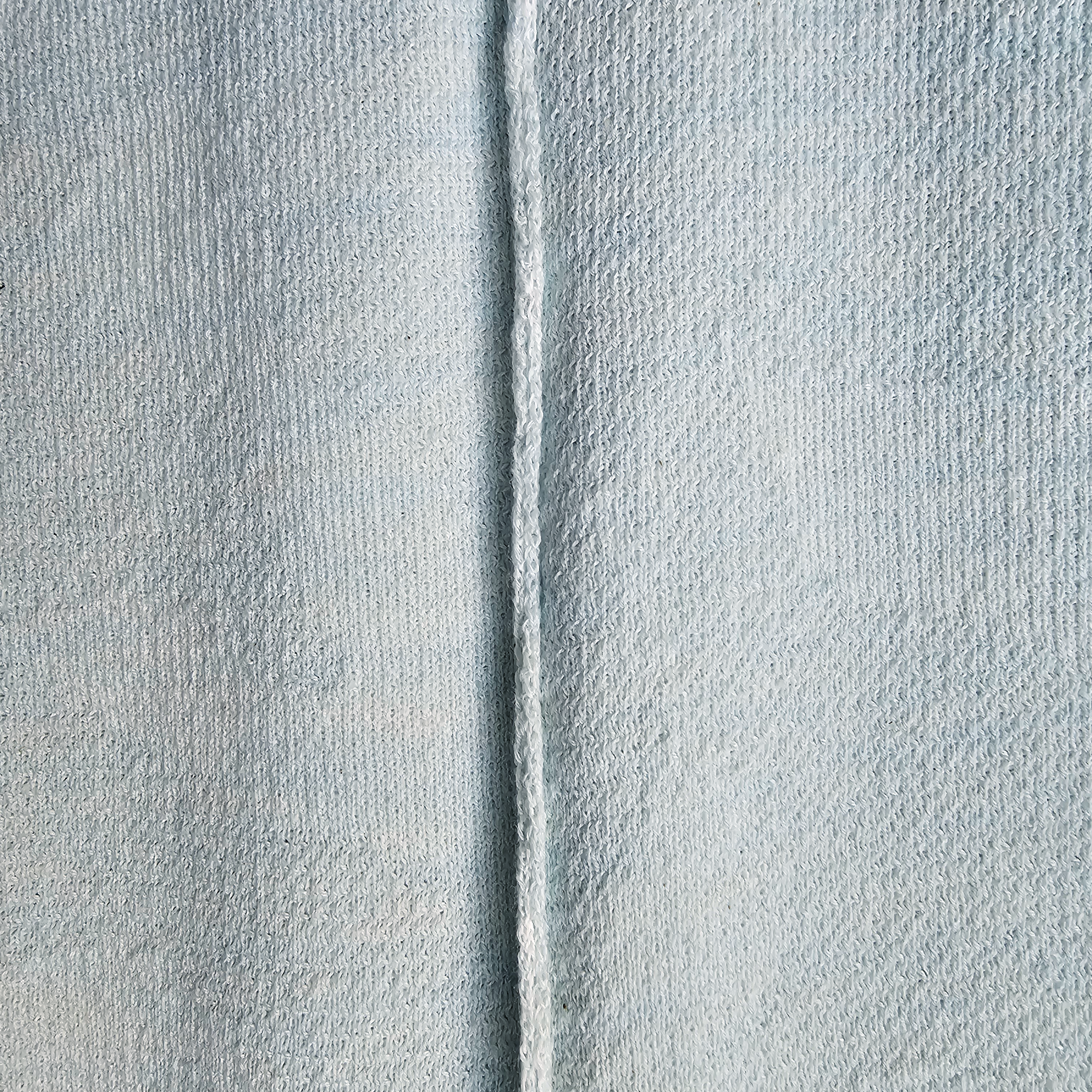 Close-up of textured light gray fabric with a vertical seam.