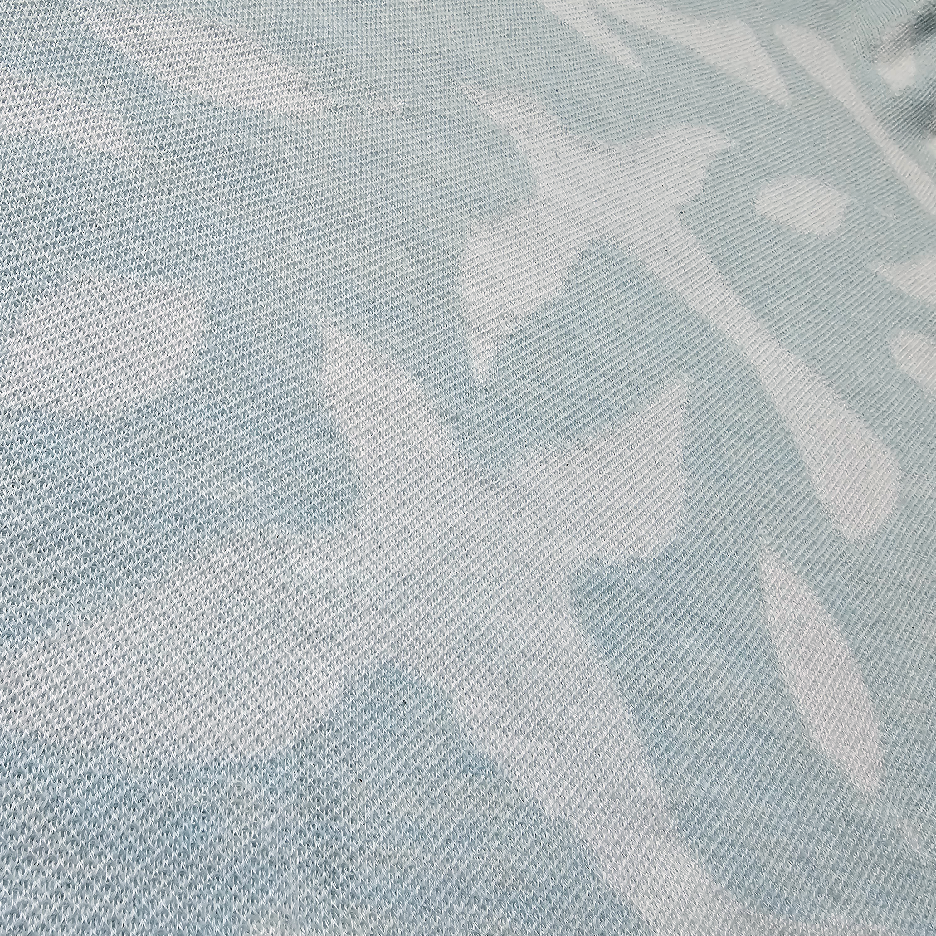 Close-up of a knitted fabric with a subtle pattern of white doves and leaves on a light blue background