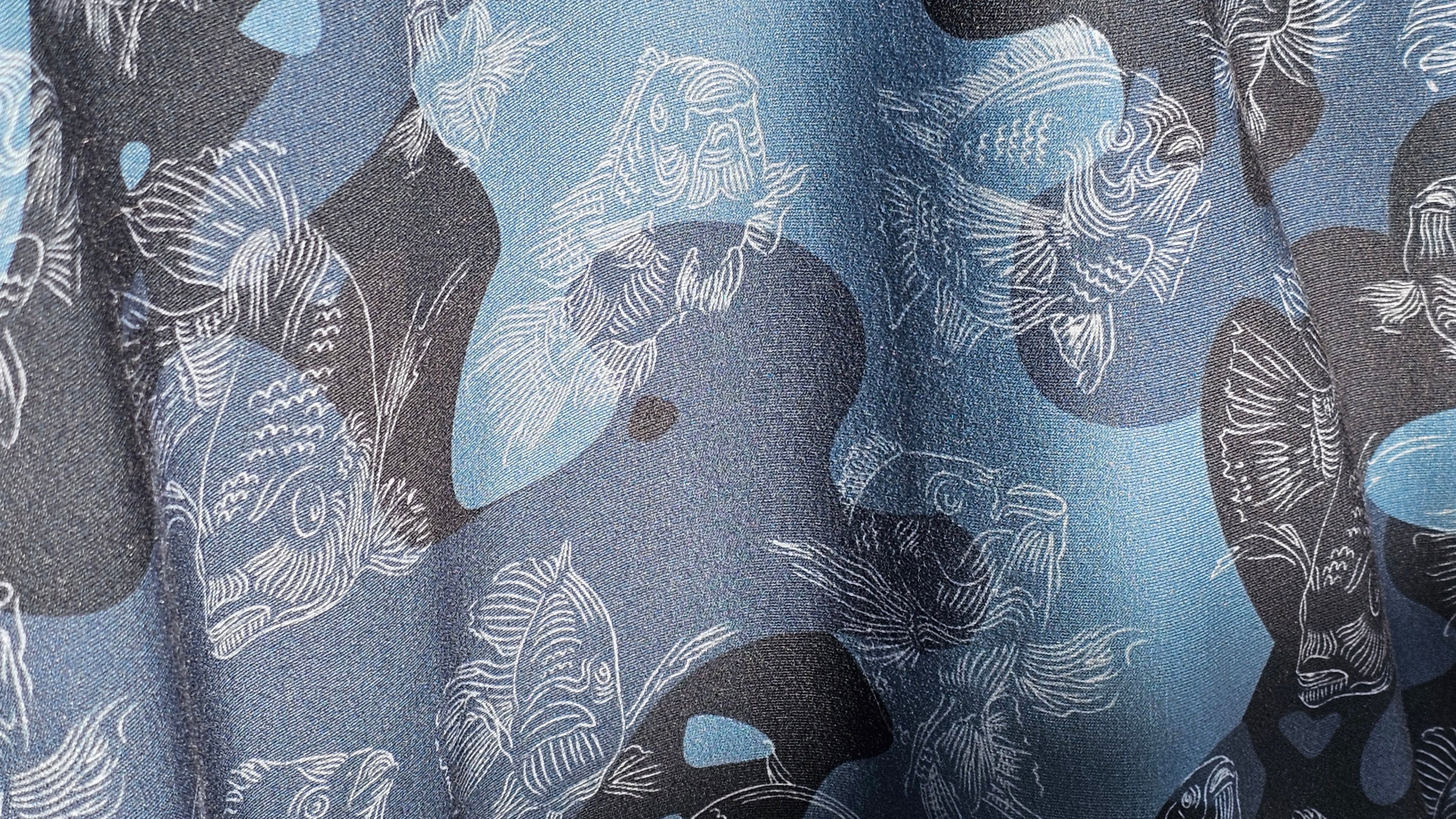 Fabric with a pattern of fish on various shades of  blue and black camouflage background