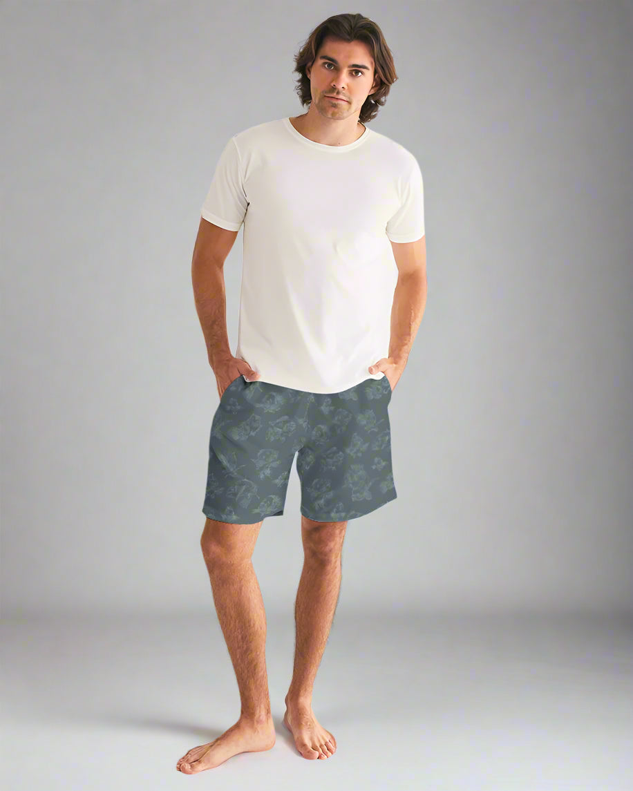 Man wearing a white t-shirt and blue patterned shorts on a plain background