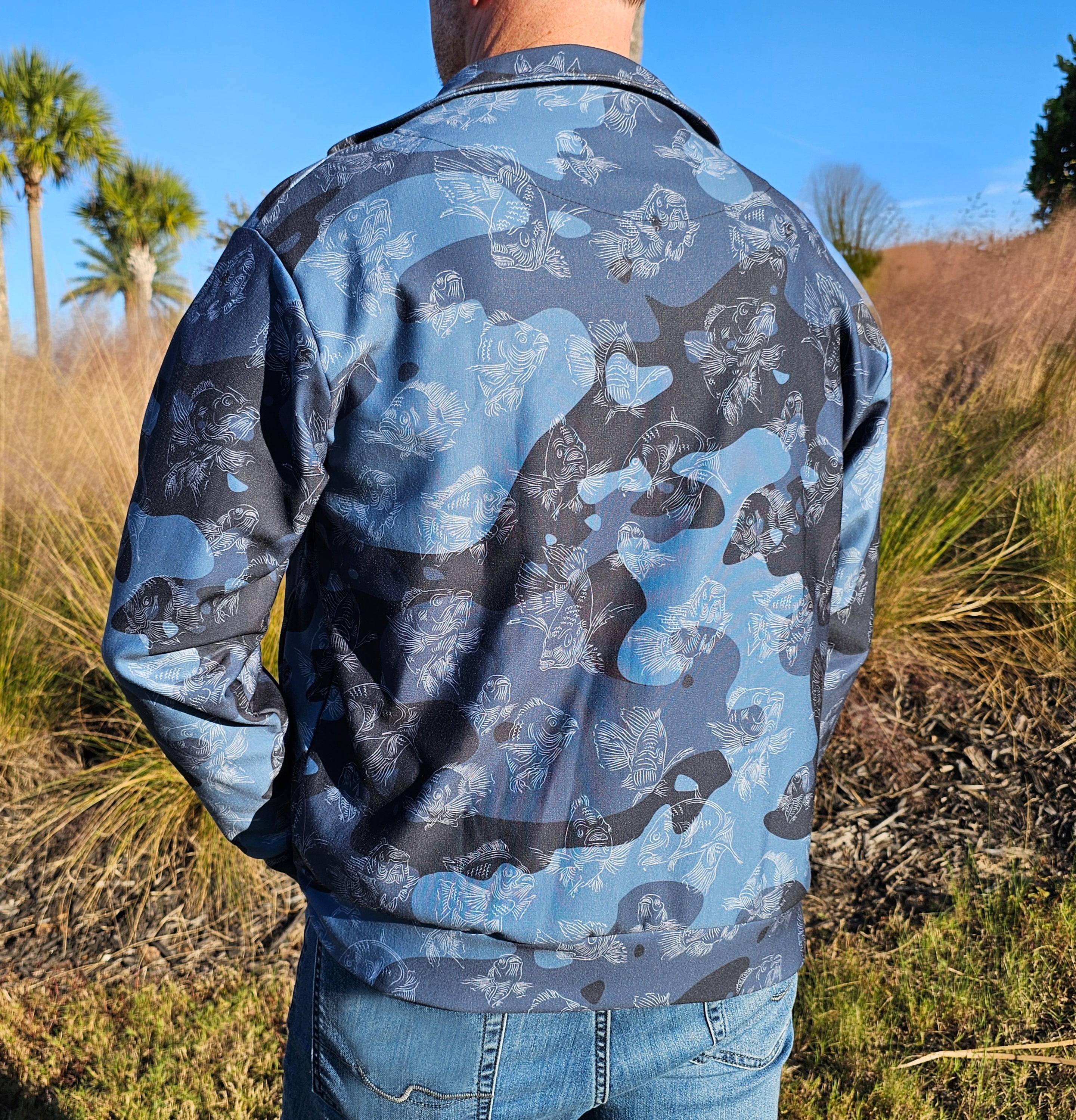 Person wearing a blue camouflage jacket outdoors with palm trees and grass in the background
