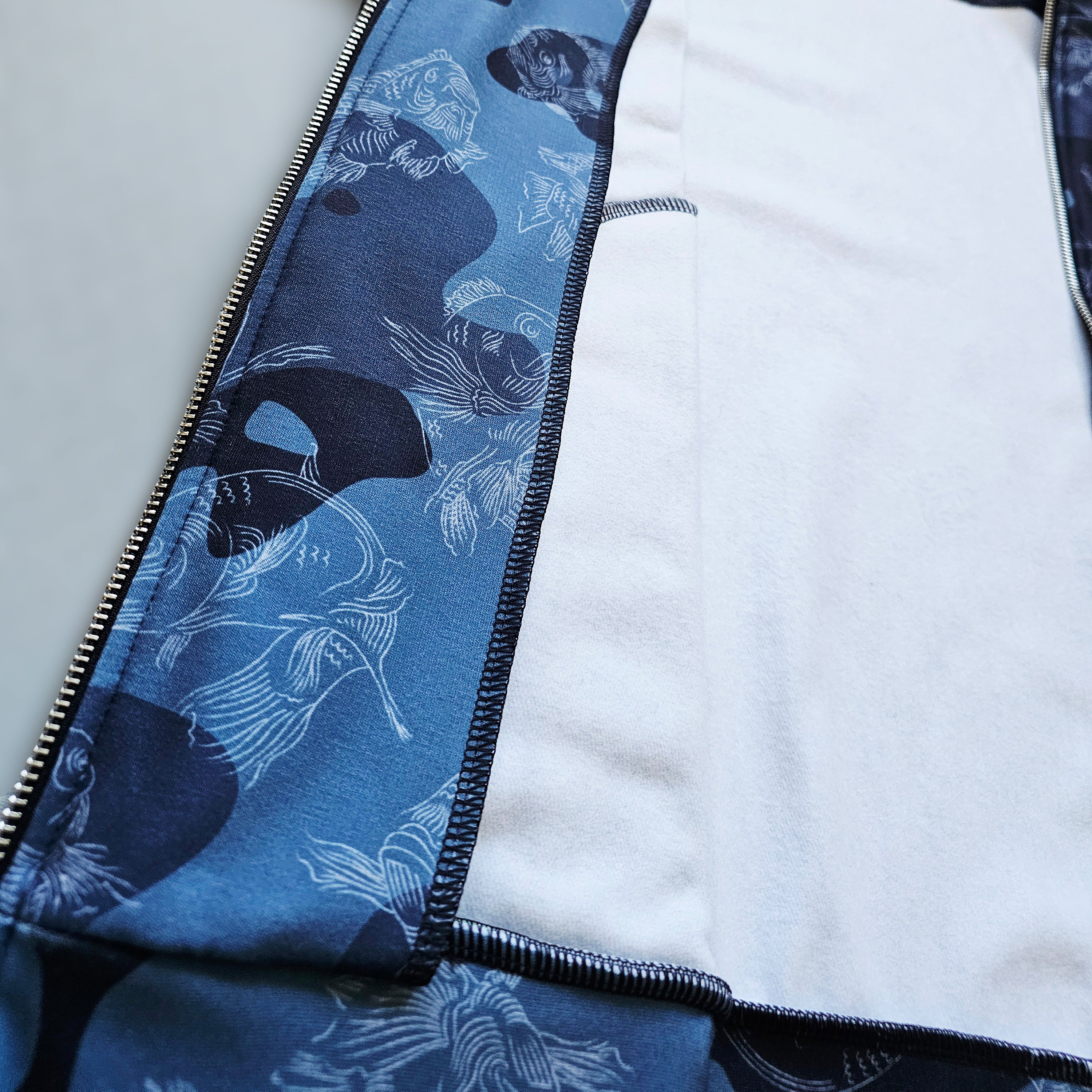 Interior fleece fabric of a blue camouflage track jacket with swimming carp pattern on a gray background 