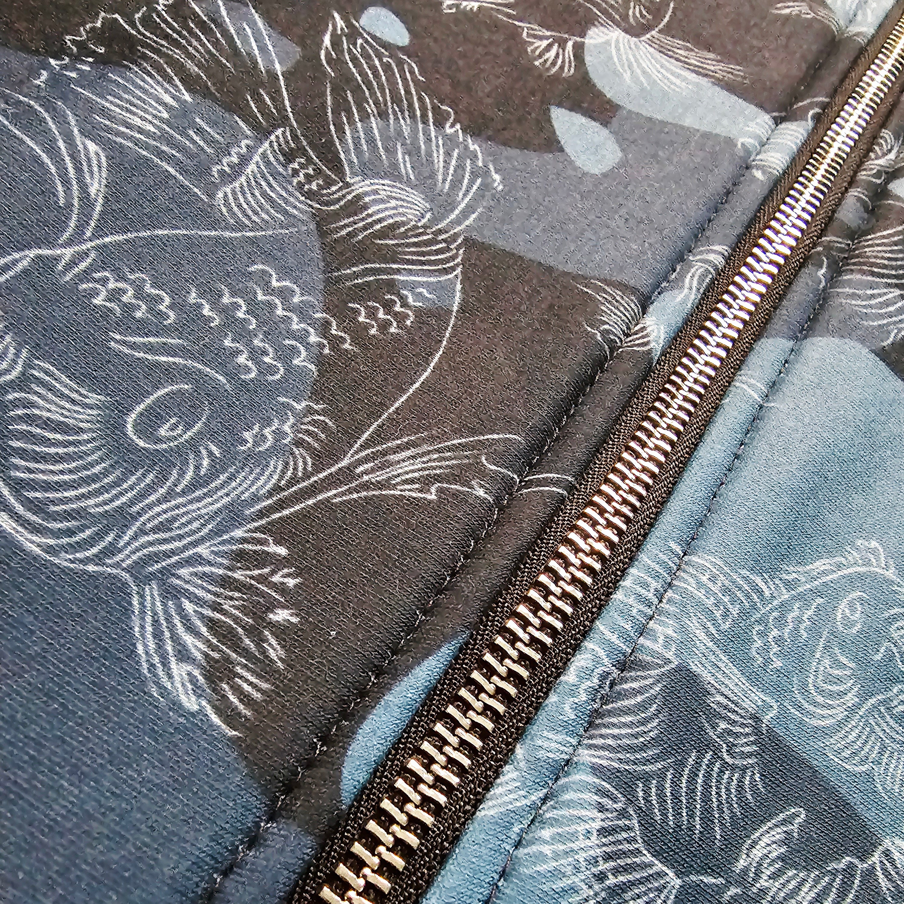 Close-up of a metal zipper on fabric with swimming carp pattern against a blue camouflage background.