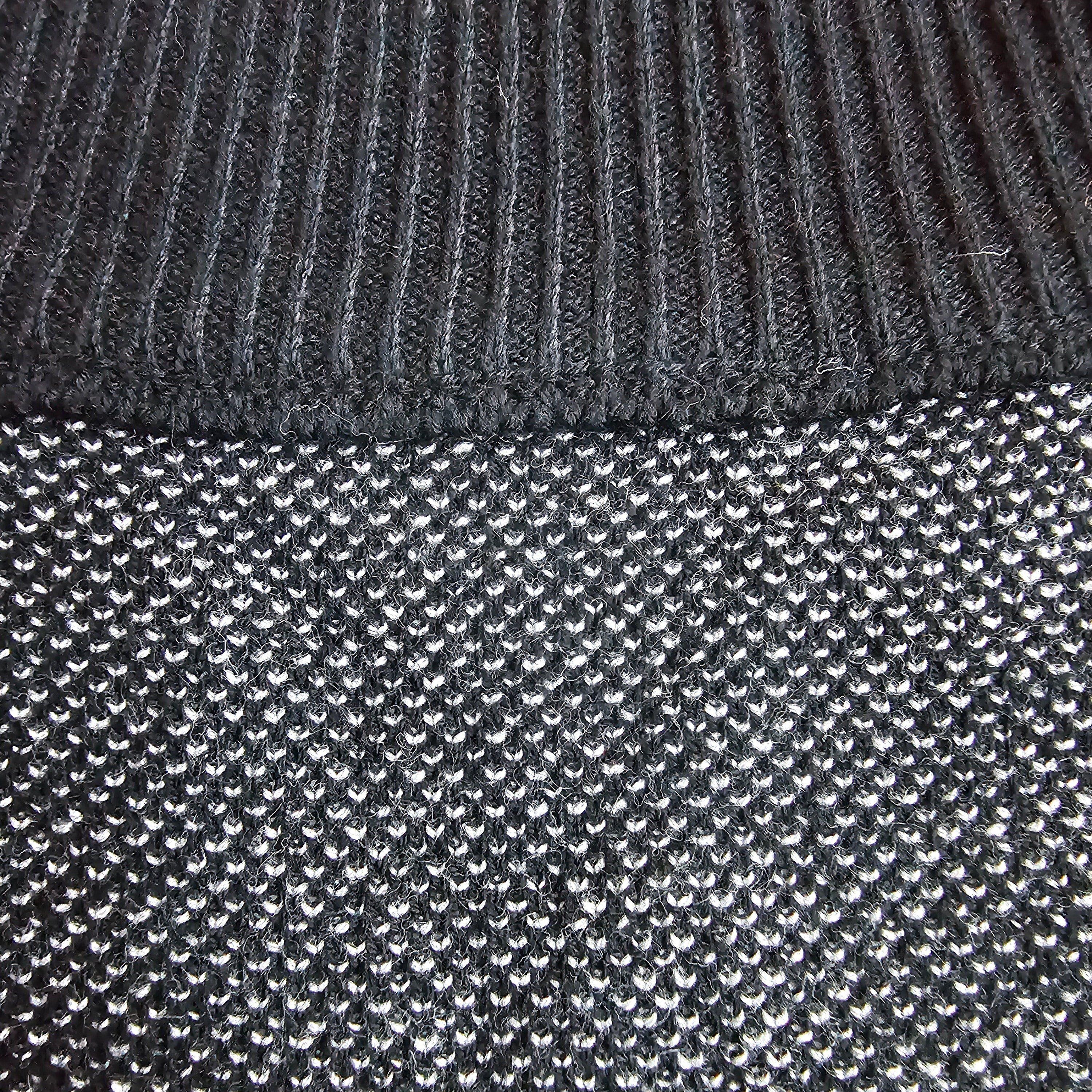 Close-up of a dark gray ribbed knit collar meeting a textured, knitted weave.