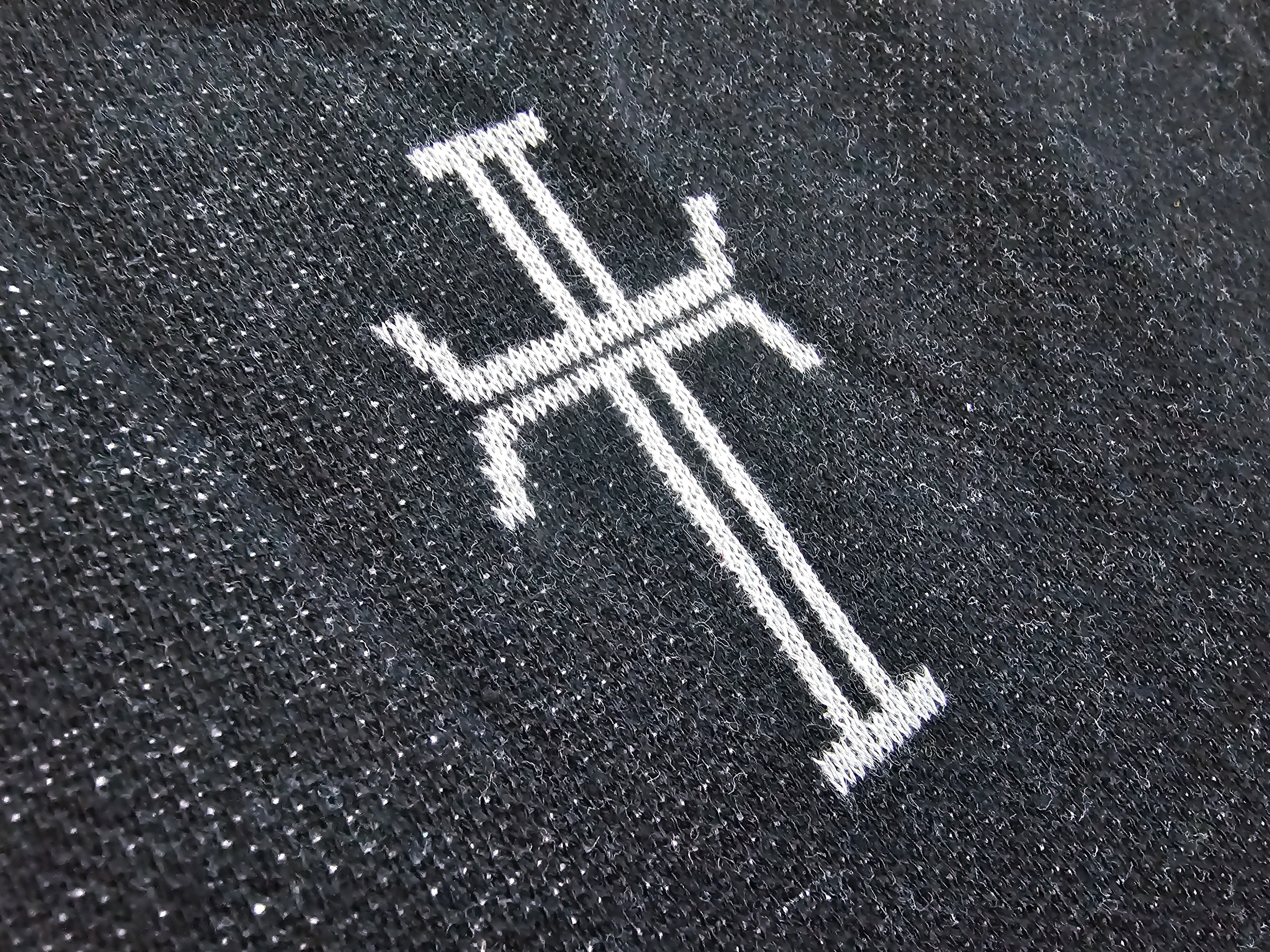 Close-up of a black knit fabric with a white knit stylized cross.