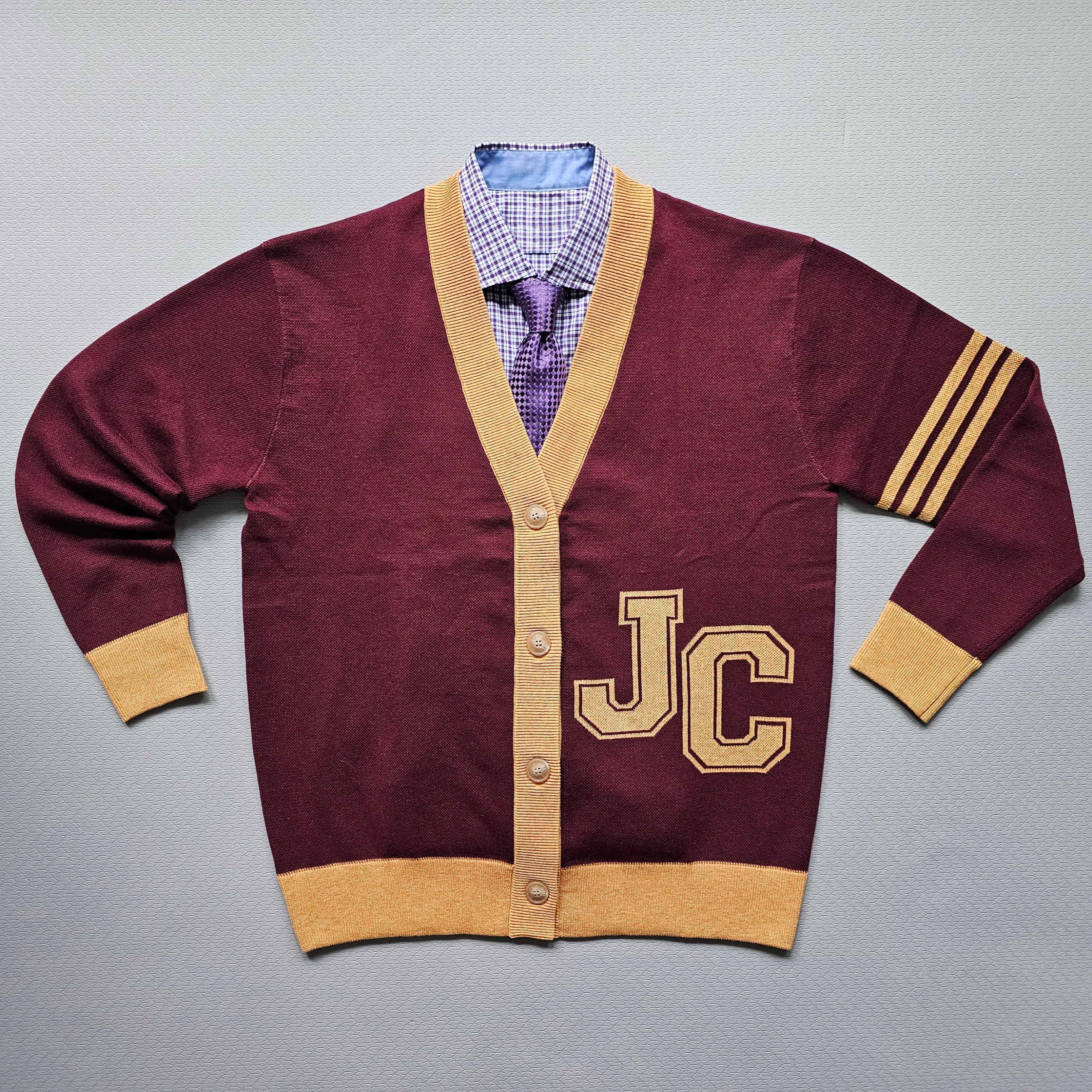 Maroon cardigan with gold trim and 'JC' lettering on a gray background
