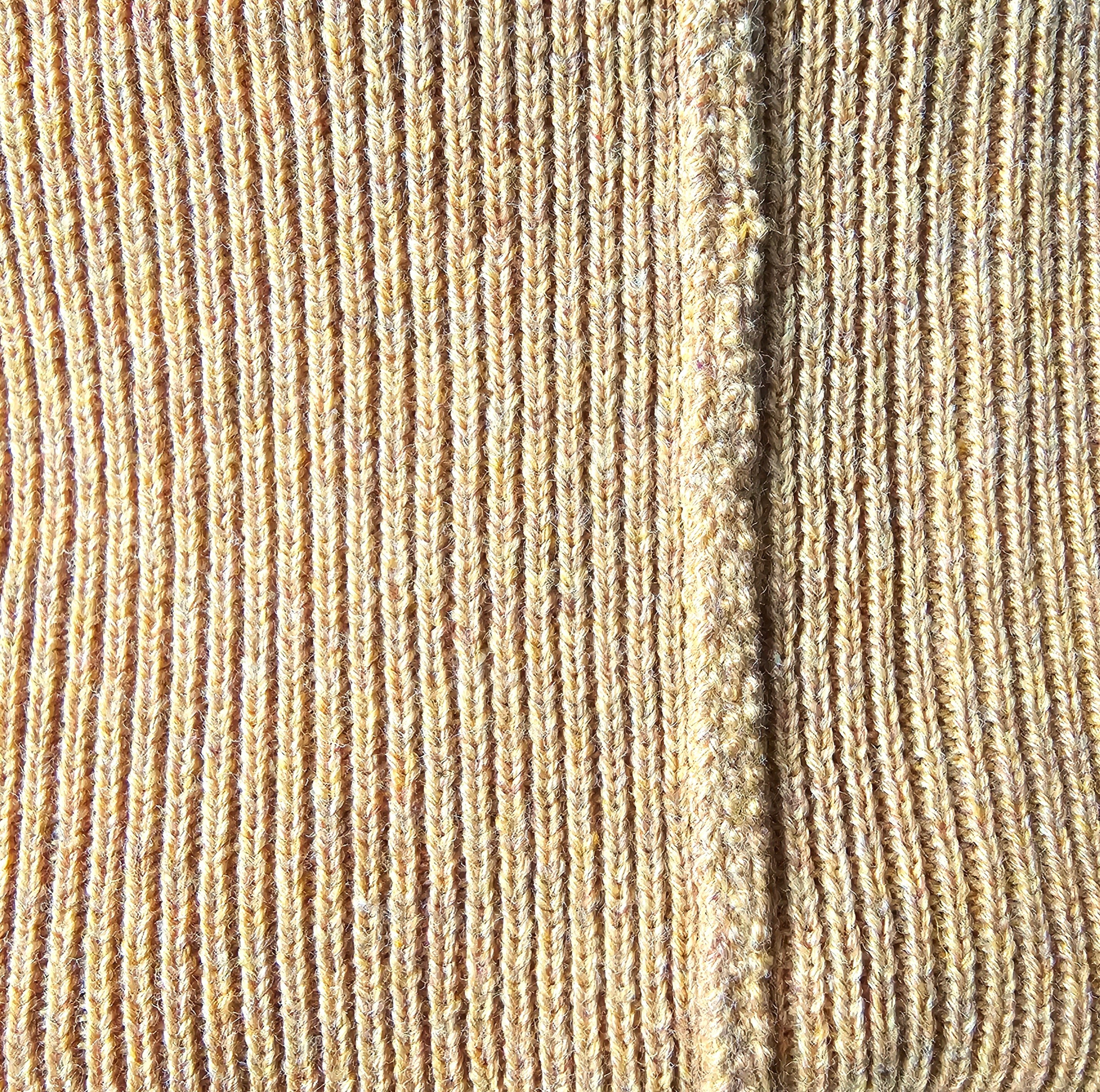 Close-up of mustard-colored textured knitted fabric with a visible finished seam.