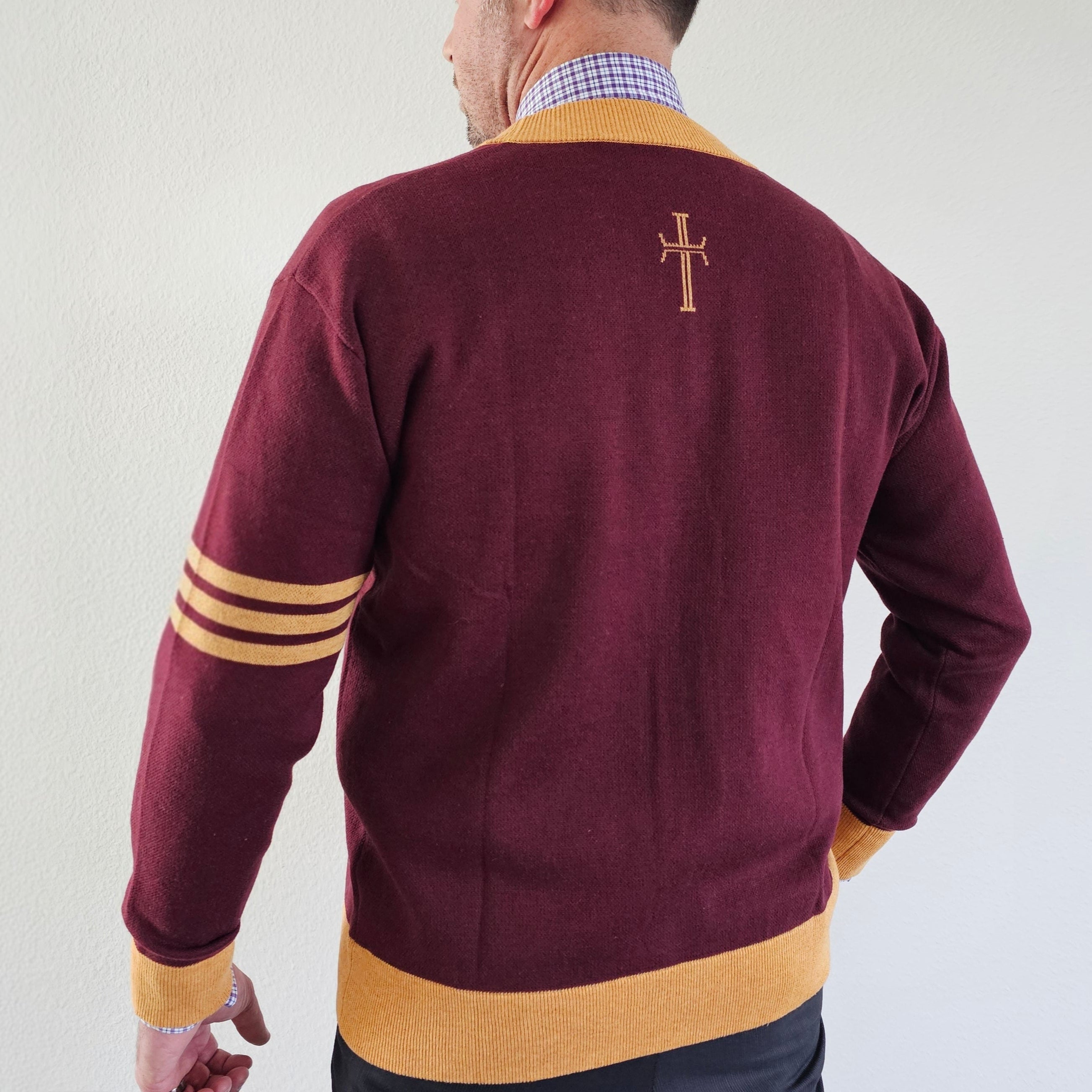 Man wearing a maroon sweater with yellow accents and a cross emblem on the back against a plain background
