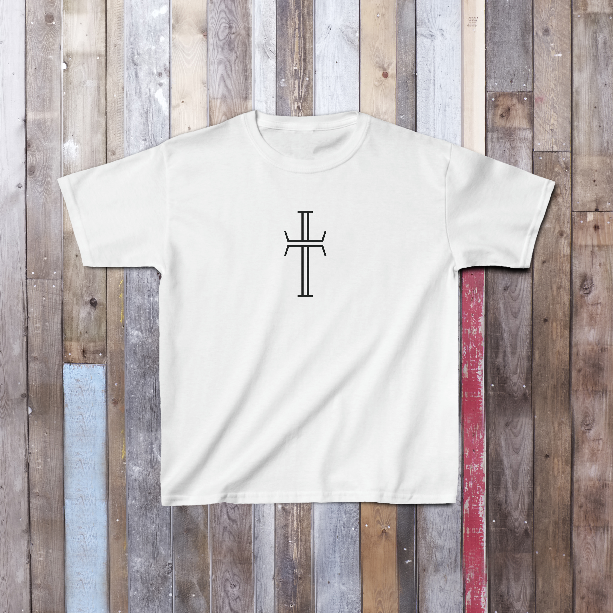 A white tee shirt with the Purpose cross logo in a bold graphic that is centered on the front chest of the garment, lays on a hardwood floor.