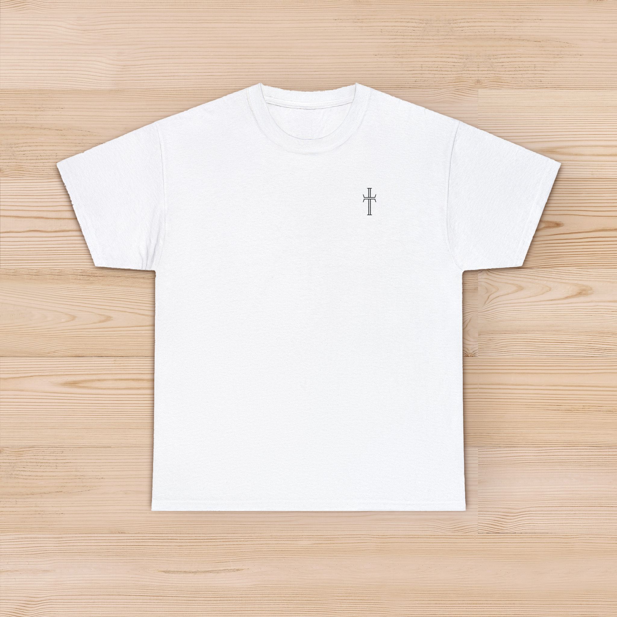 A white tee shirt lays against a pine hardwood floor, displaying the front of the garment with the Purpose cross in black on the left chest.