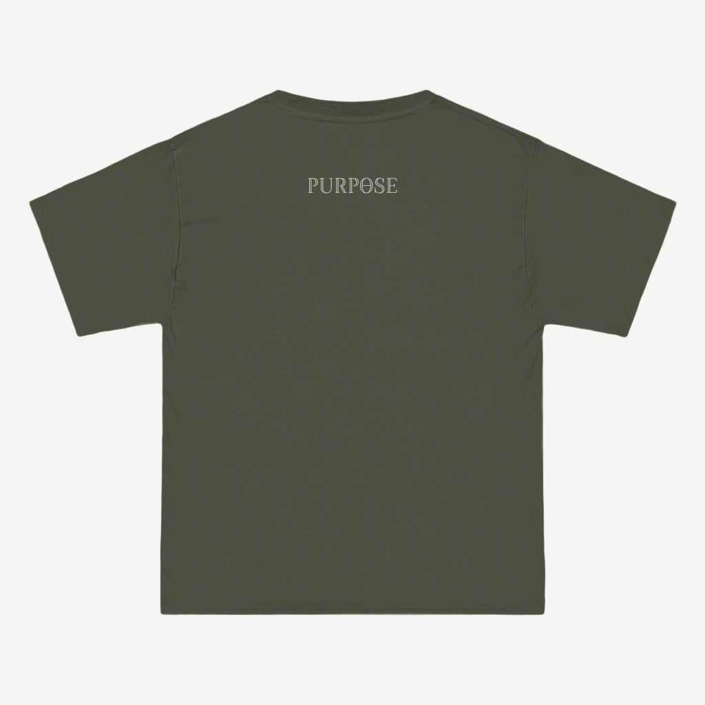 A roomy army green crewneck tee shirt displays the back of the garment as it lays against a painted brick-patterned wall. The Purpose worded logo is printed in white along the top center.