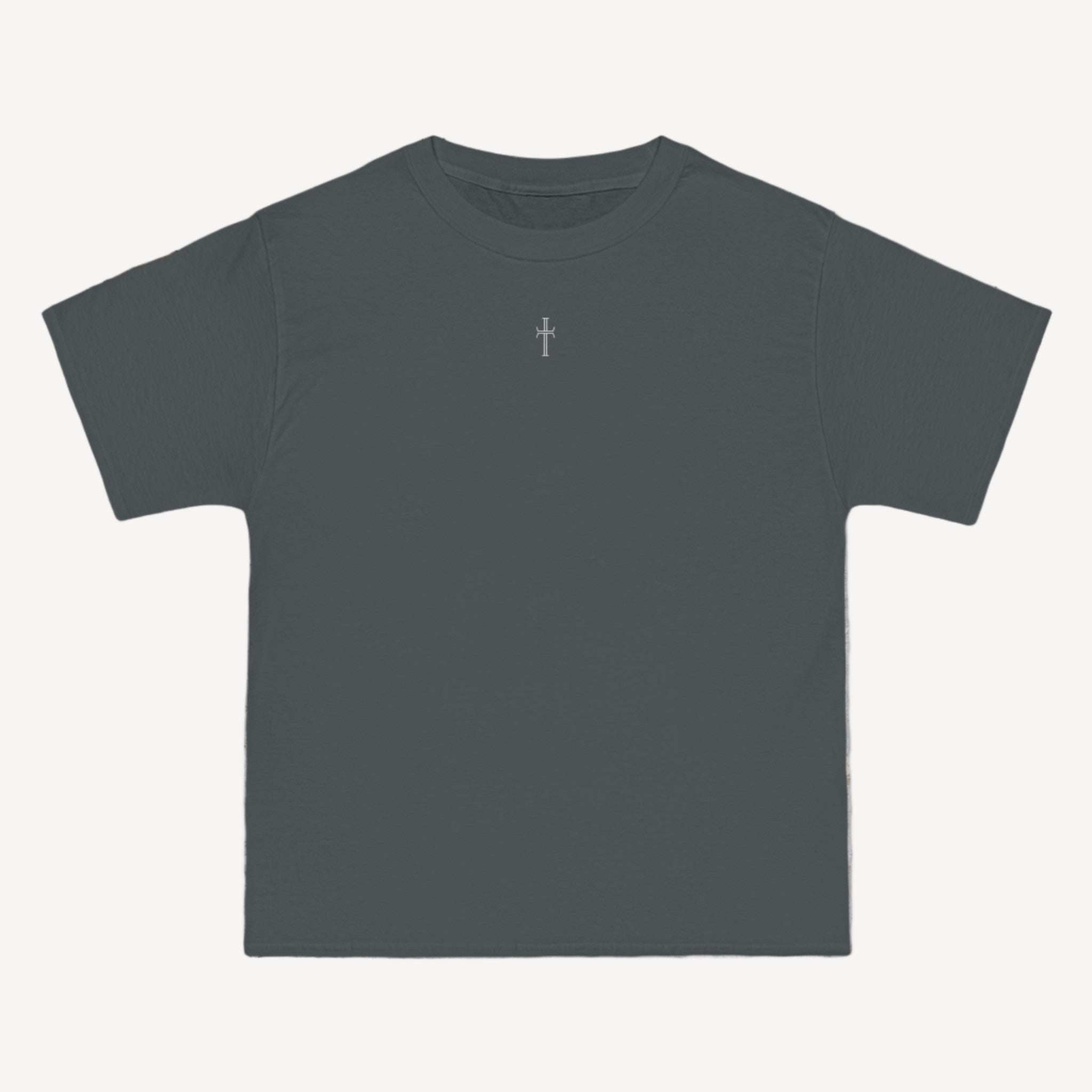 A gray crewneck tee shirt displays the front of the garment as it lays against a brick-patterned wall. A small white Purpose cross logo is printed at the top center. 