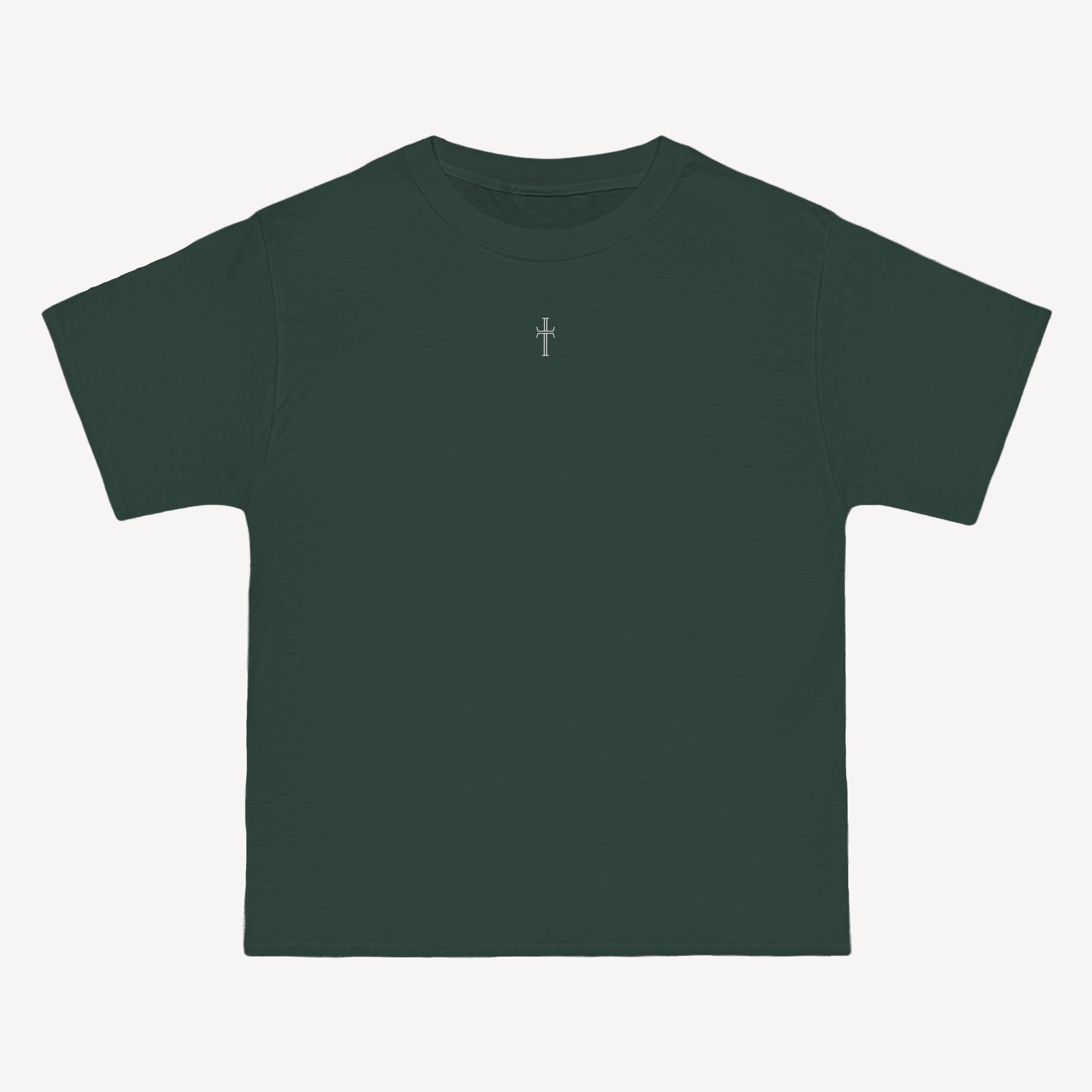 A forest green crewneck tee shirt displays the front of the garment as it lays against a brick-patterned wall. A small white Purpose cross logo is printed at the top center. 