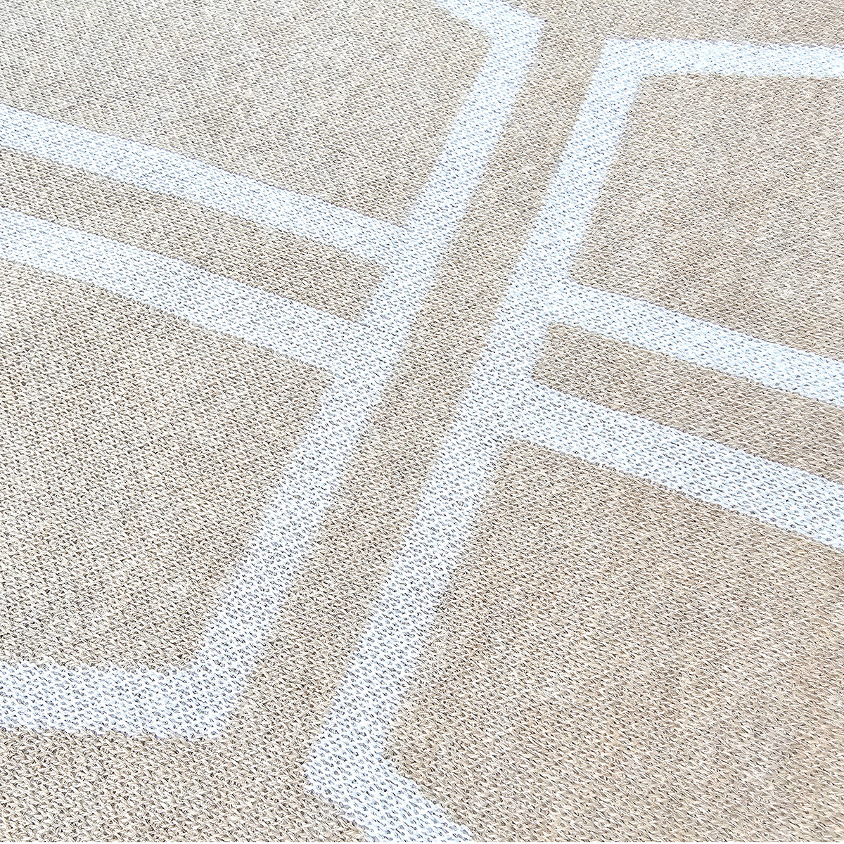 An angled close-up of the white knitted crucifix graphic of the beige sweater.