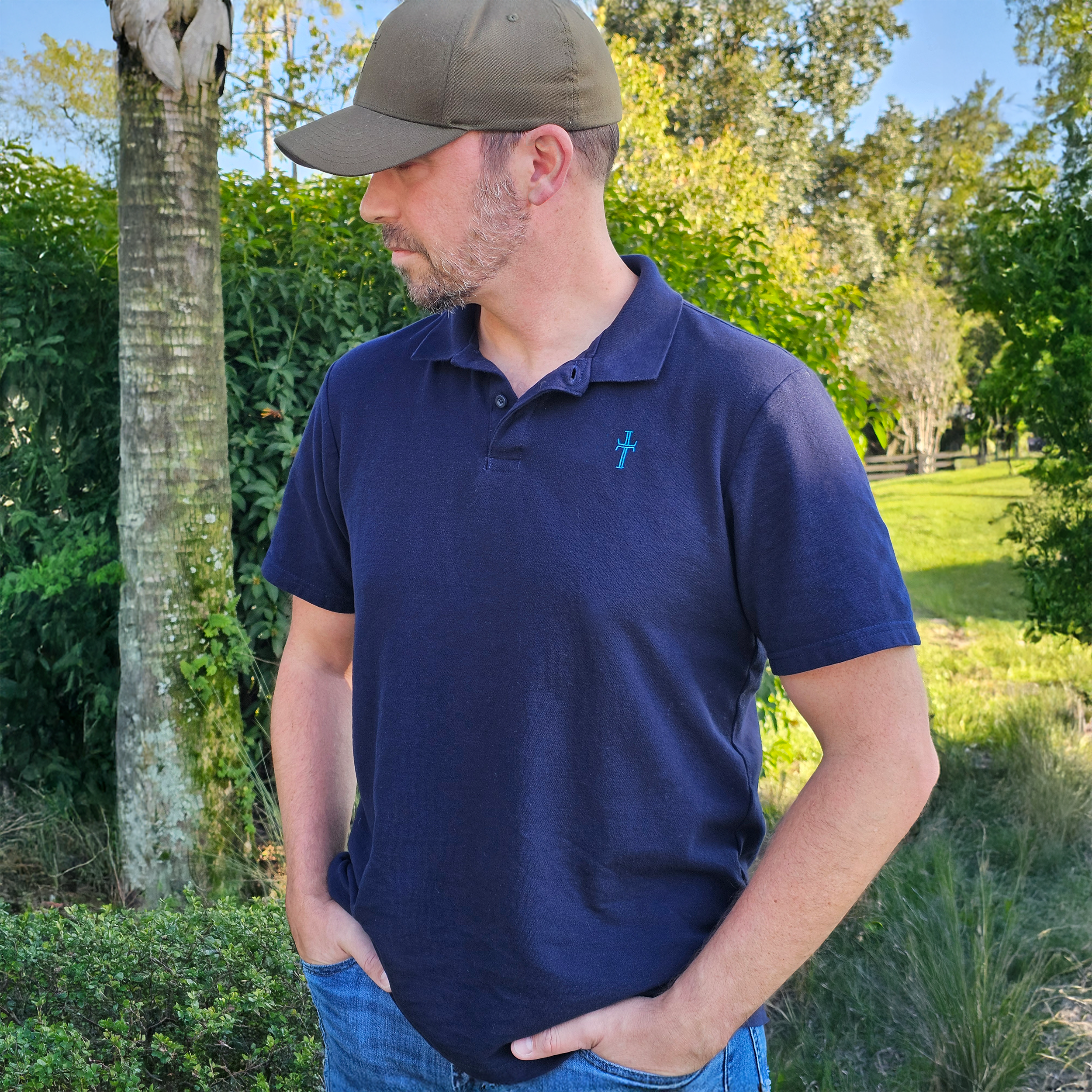 Man wearing a navy blue polo shirt with a logo, standing outdoors in a garden.