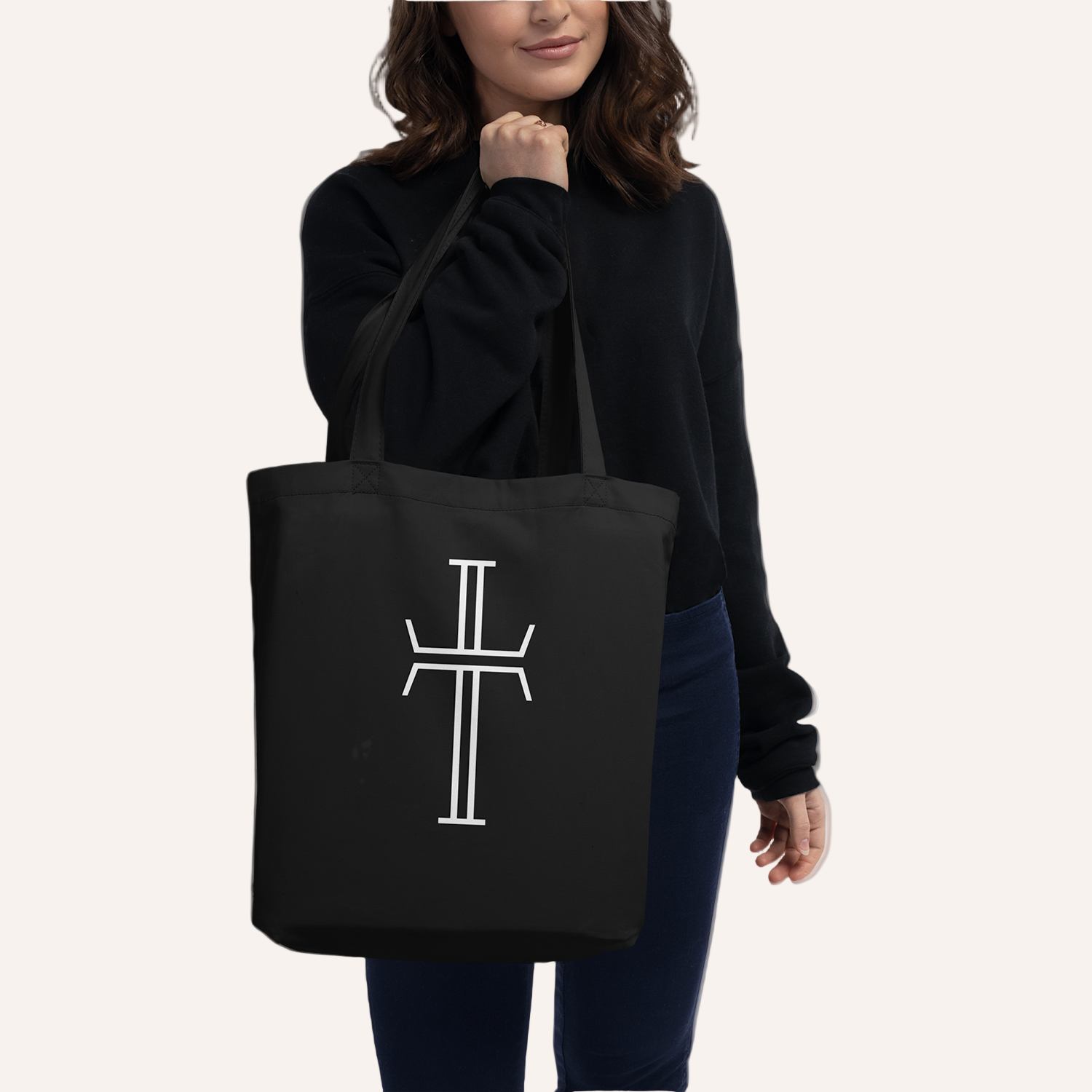 A female model holds a black tote bag with a large white Purpose cross logo. The bag has long double handles.