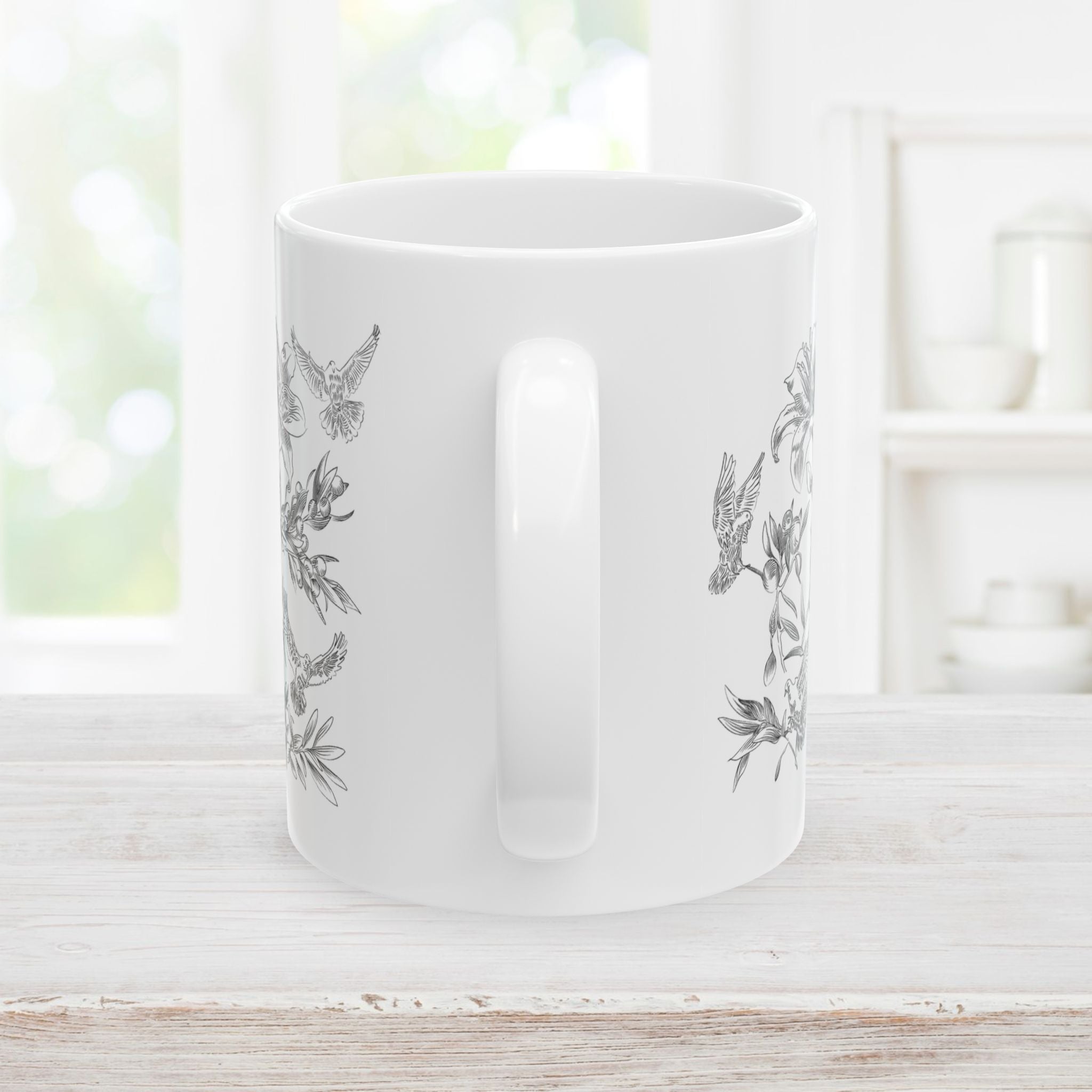 Back side and handle of white mug with black floral and dove pattern on a light wooden surface.