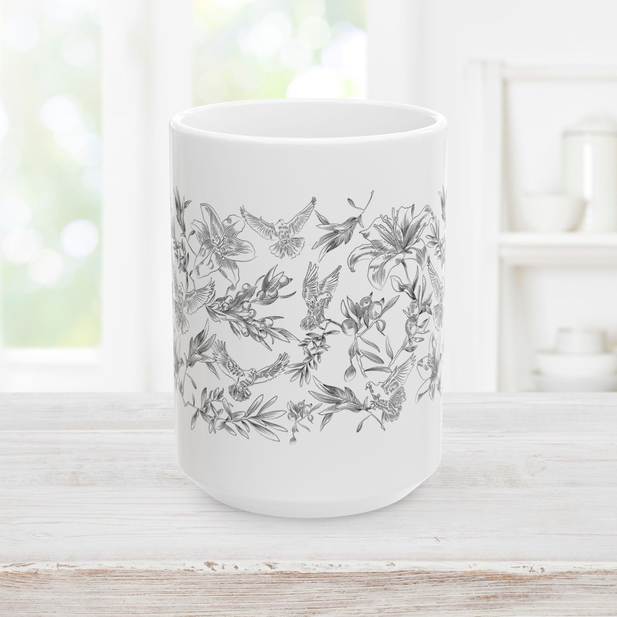 Front side of white ceramic mug with black floral and dove pattern on a light wooden surface.