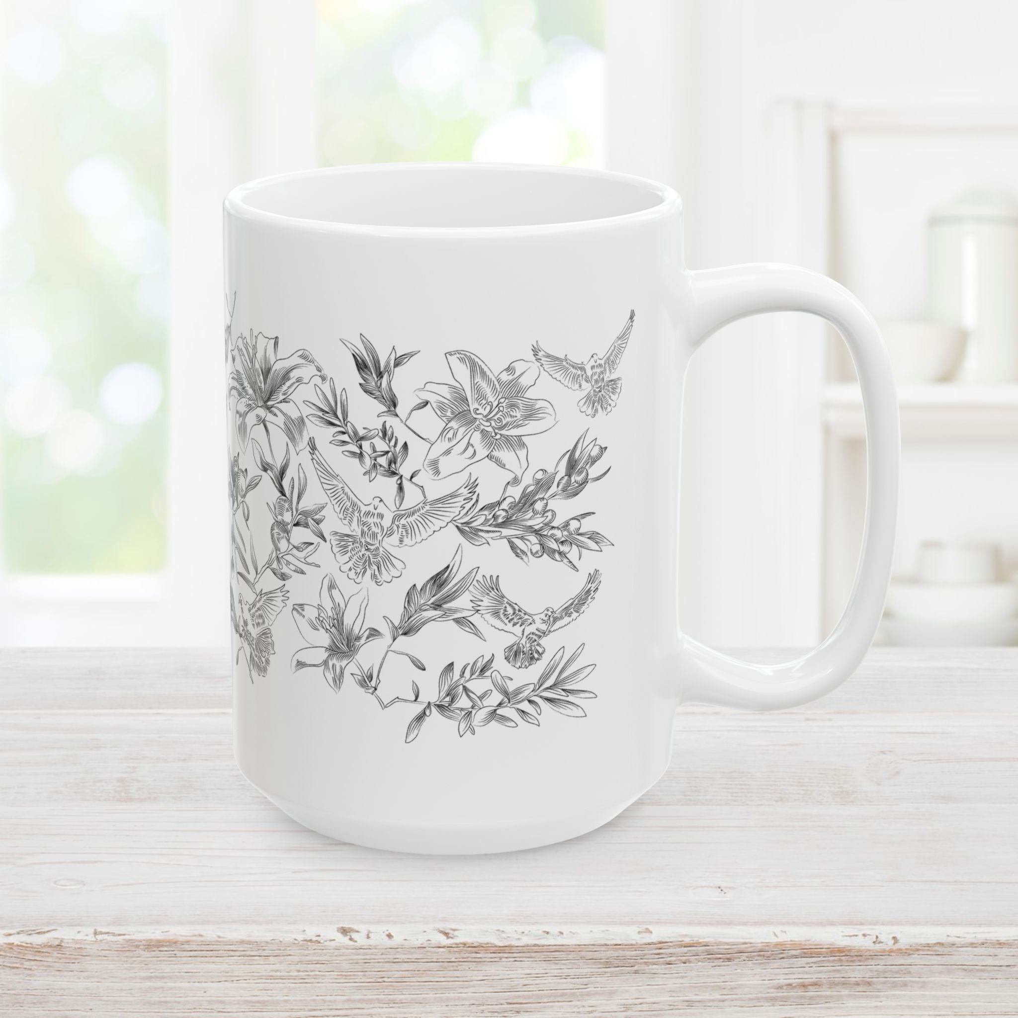 Left side of white mug with black floral and dove design on a light wooden surface.