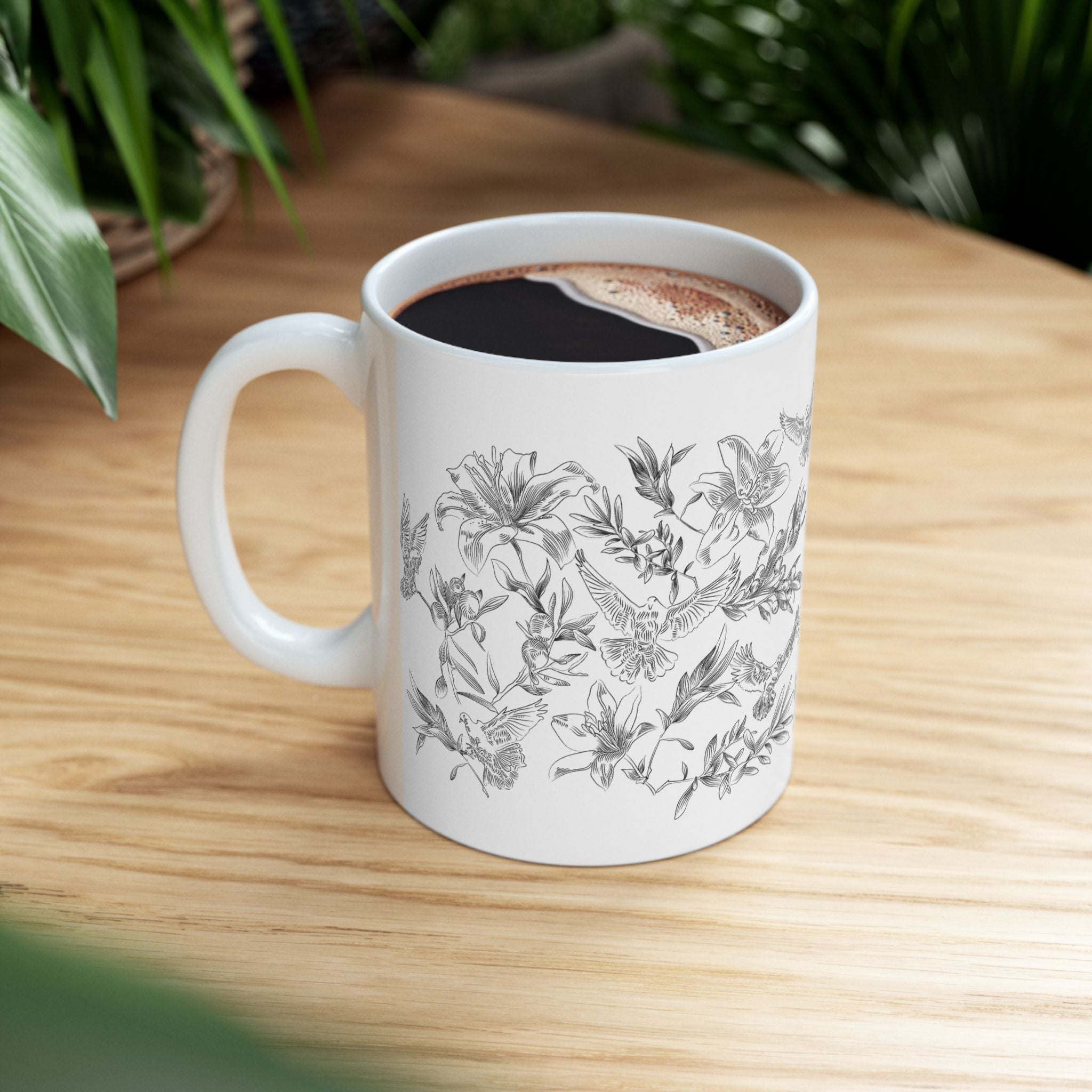 White mug with black floral and dove design on a wooden surface.